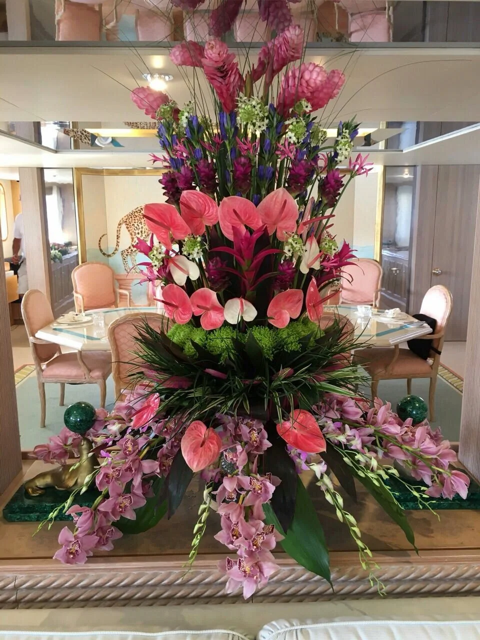 Large floral arrangement with pink, purple, and green flowers on a dining table in a restaurant setting.