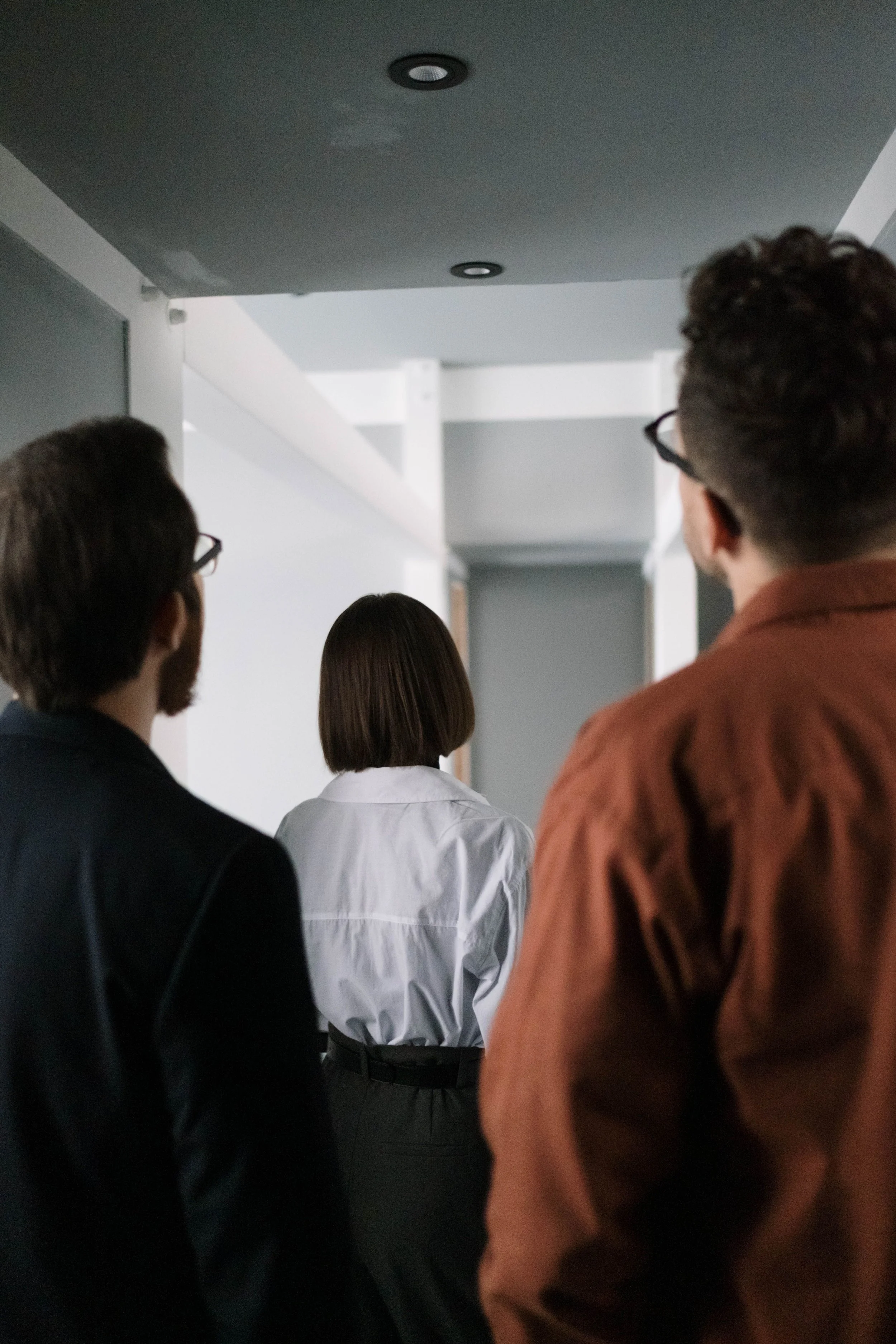 People standing in a line or group in an indoor setting, viewed from behind.