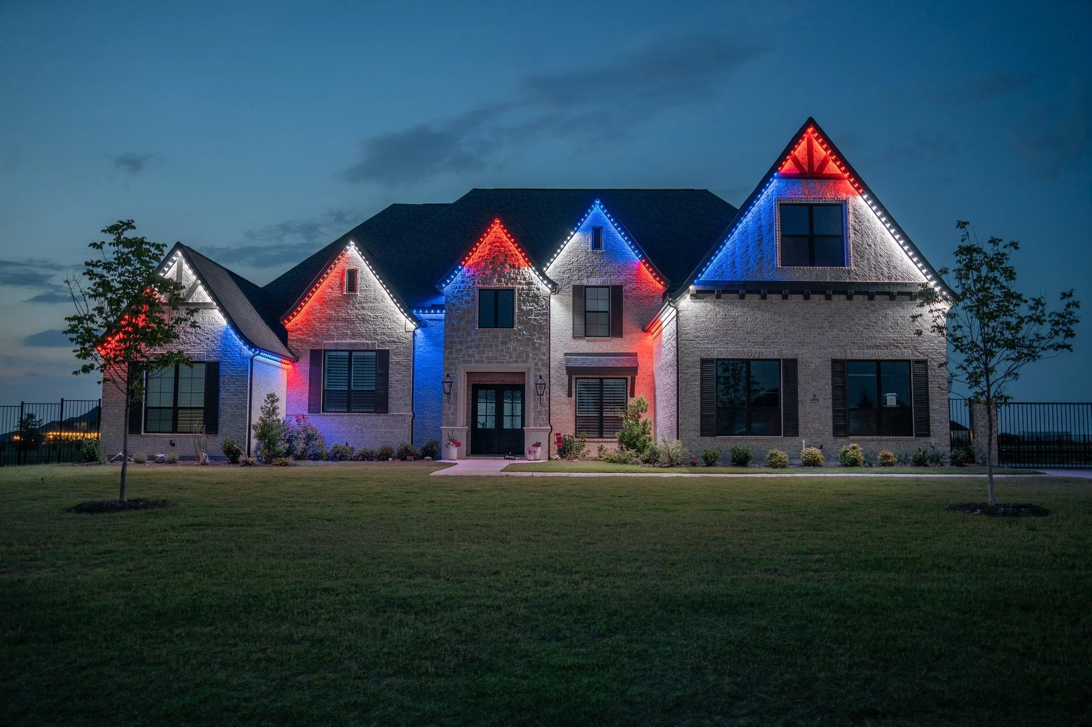 A house decorated with red, white, and blue Christmas lights on its gabled roof at dusk.