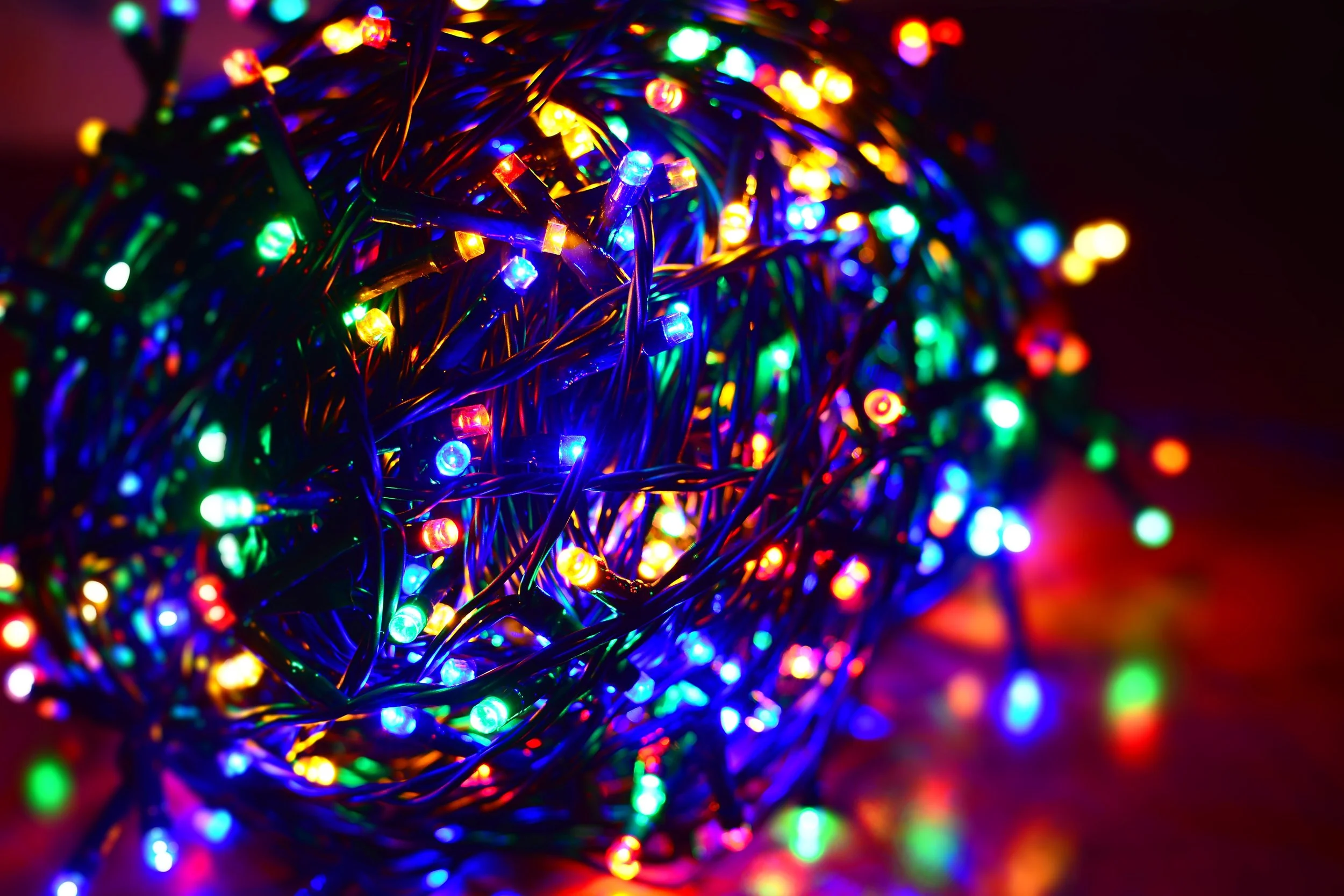 A bunch of colorful LED Christmas string lights tangled together, glowing in various colors including red, green, blue, and yellow, against a dark background.