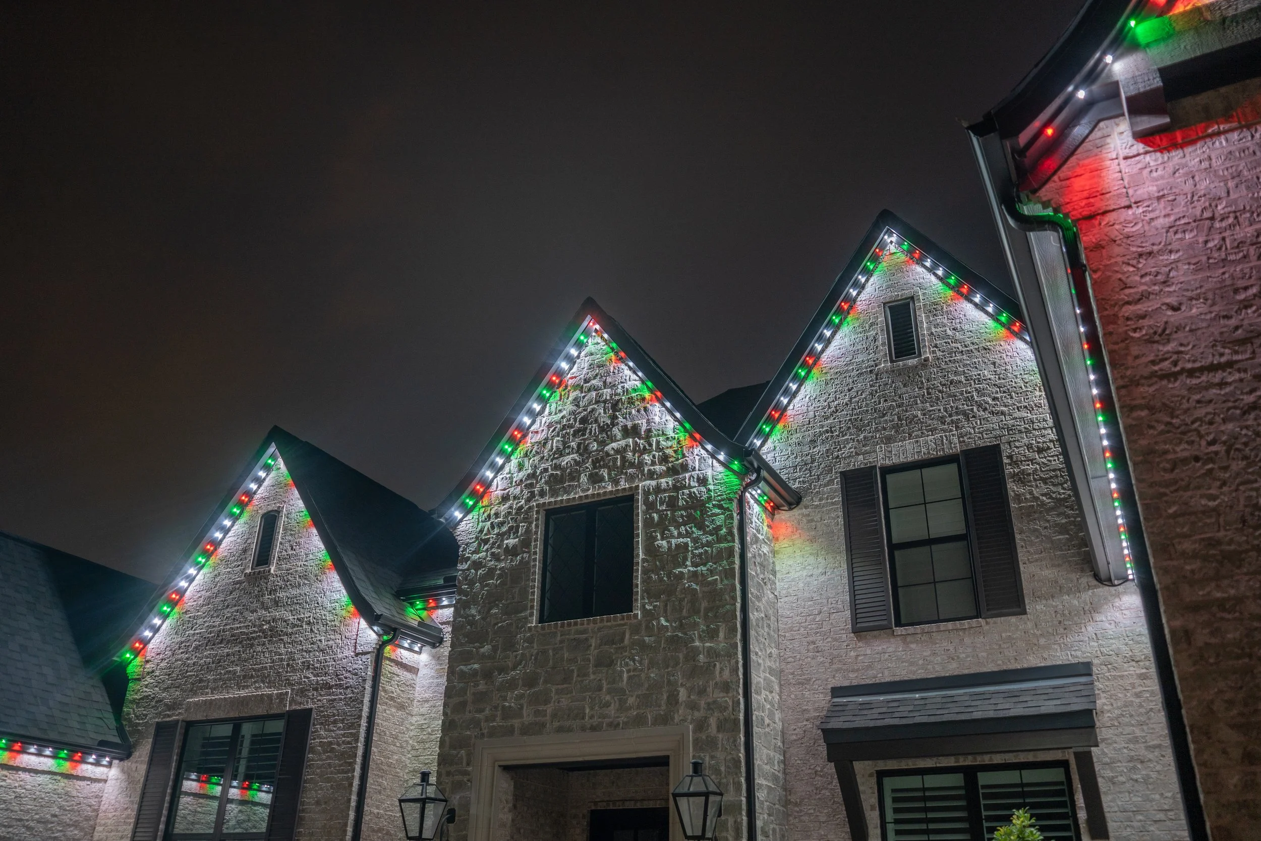 Nighttime view of a house decorated with multi-colored Christmas lights along the rooflines and windows.