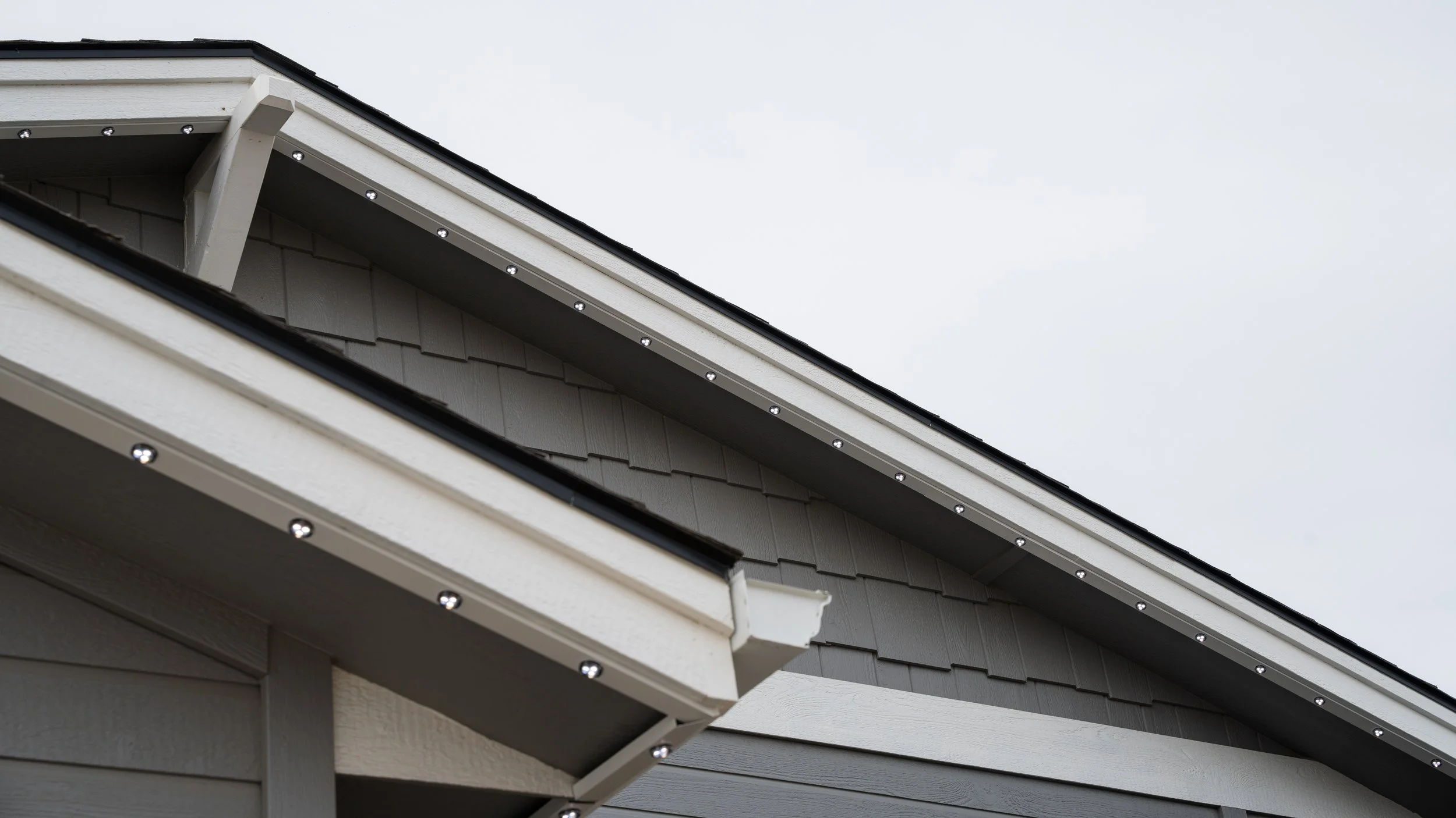 Close-up of a house's roof and gutter with visible screws, against a cloudy sky.