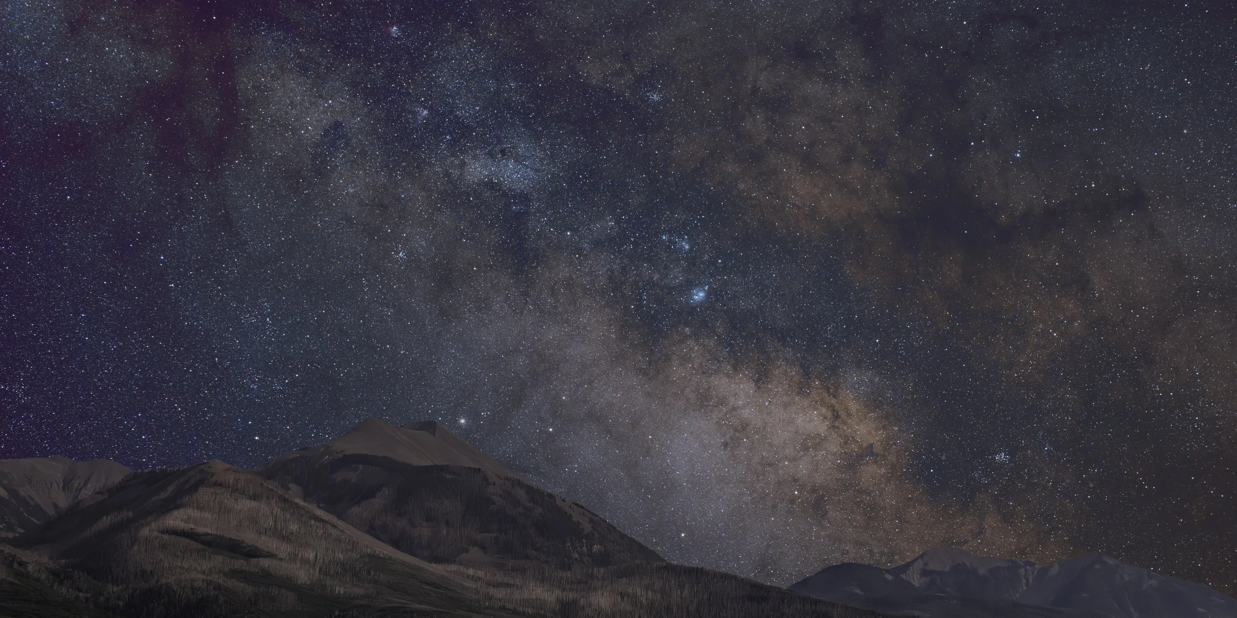 Night sky filled with stars and the Milky Way galaxy above mountain range.