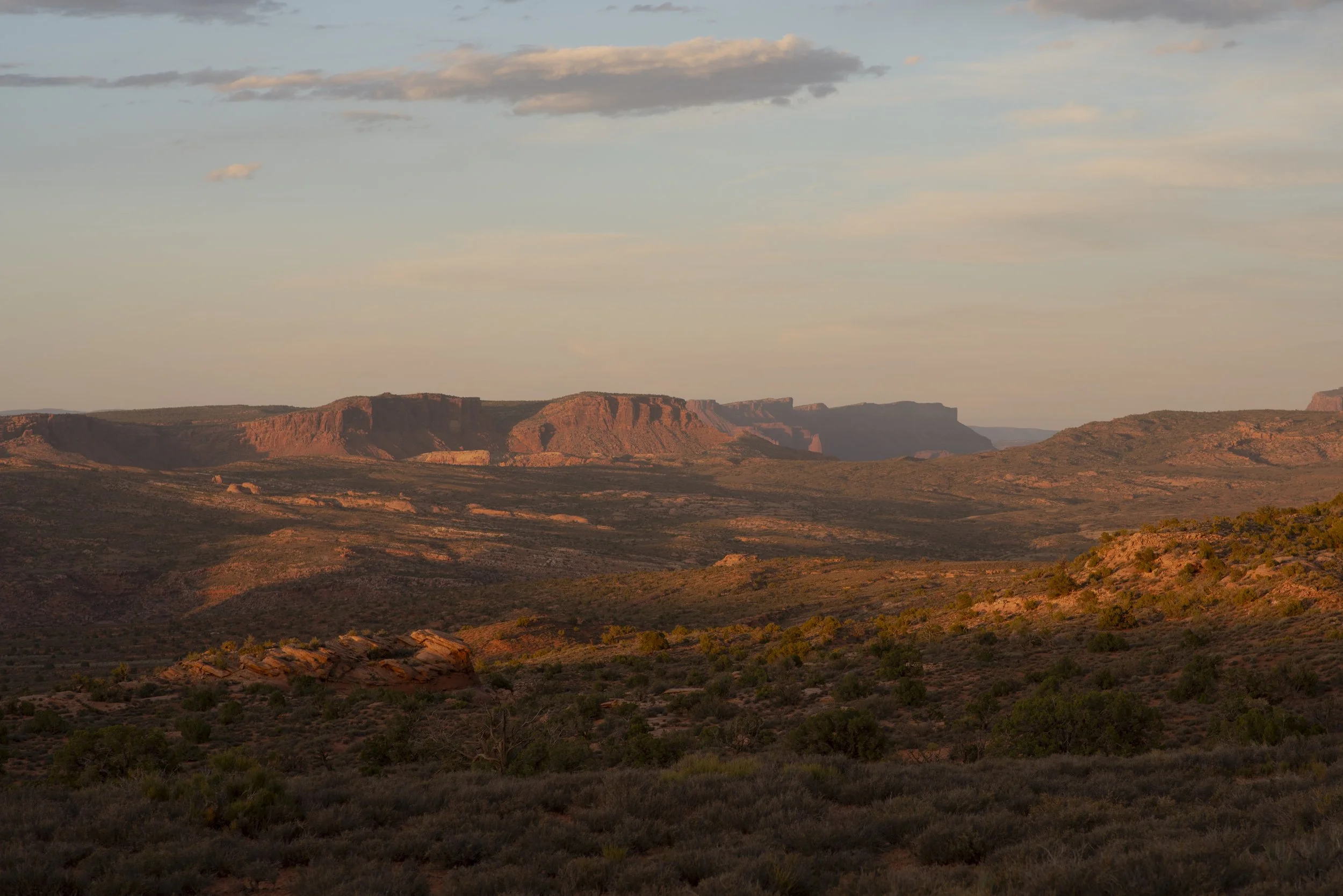 A desert landscape at sunset in Arches National Park with red rock formations and an amber light blue sky.