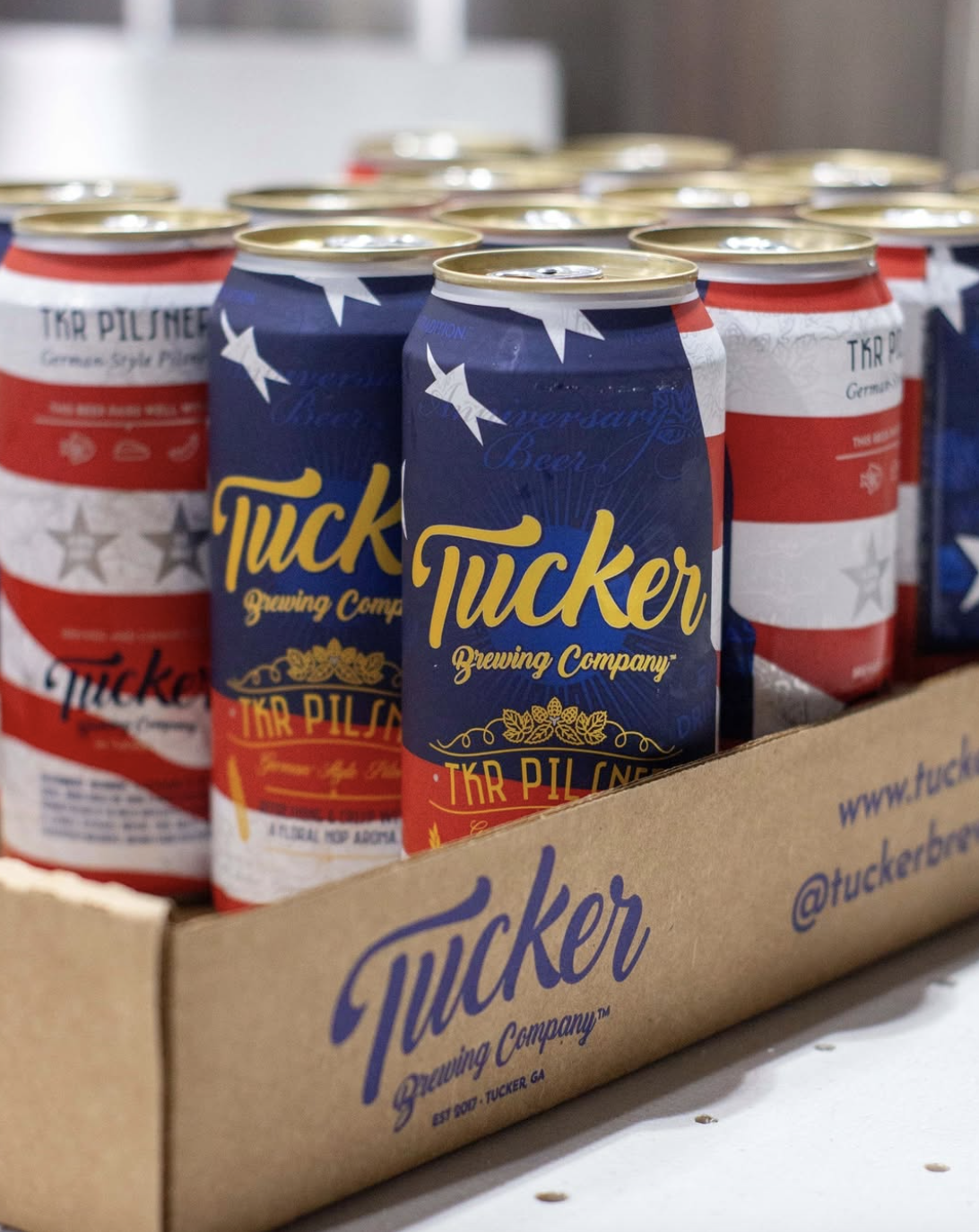 Cans of beer with patriotic red, white, and blue labels in a cardboard tray on a white surface.