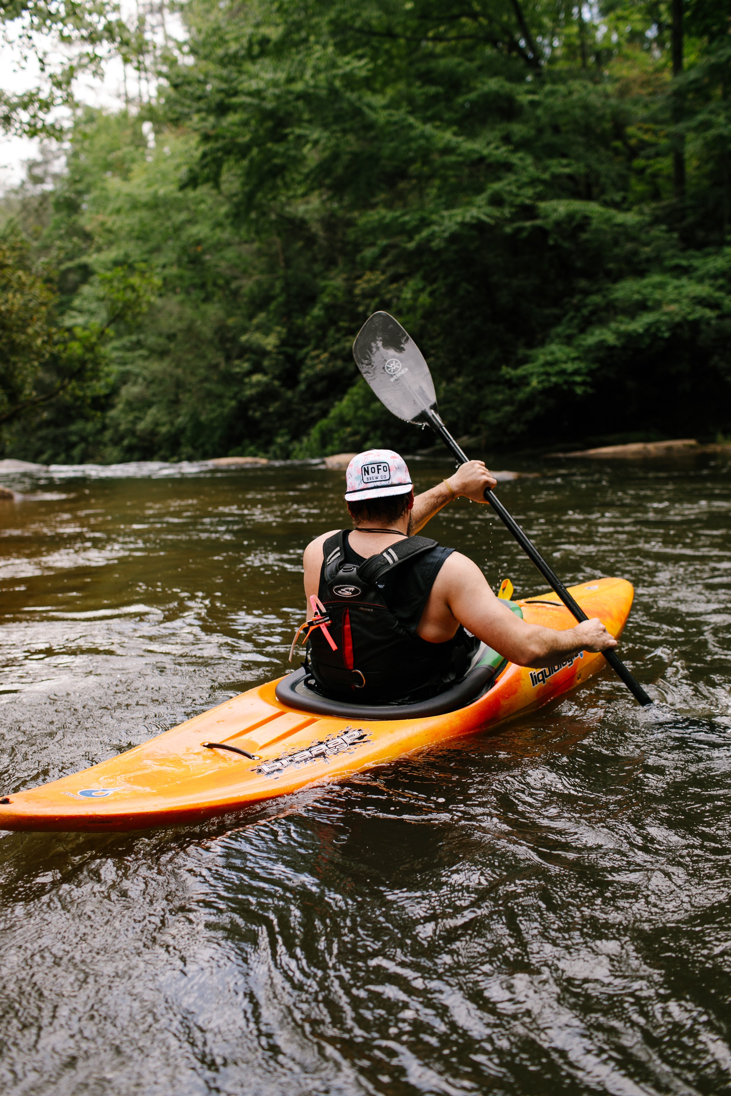 A person kayaking on a river surrounded by lush green trees.