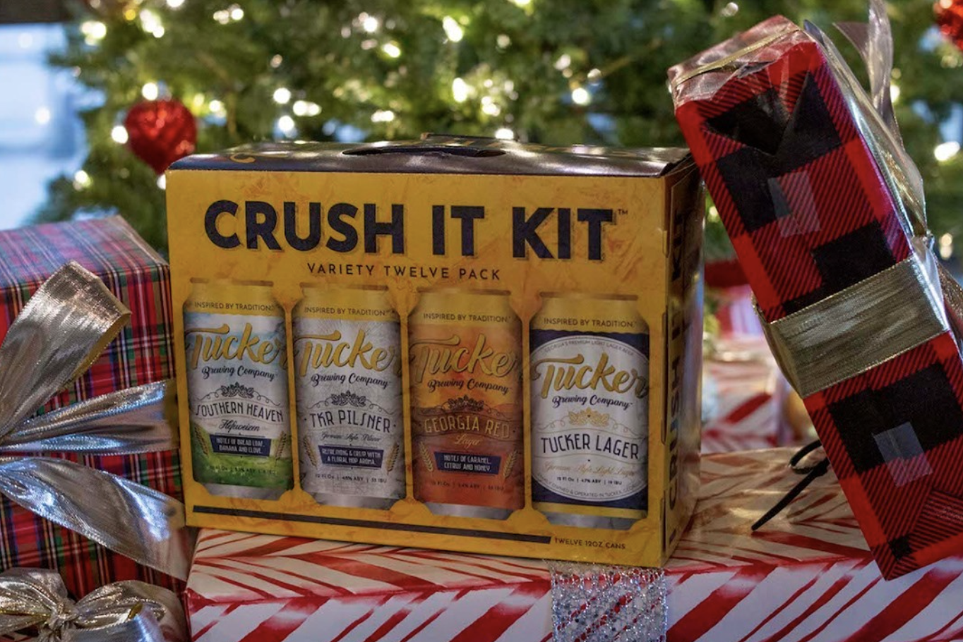 Box of Craft Beer variety pack with four canned beverages, surrounded by wrapped presents and Christmas decorations.