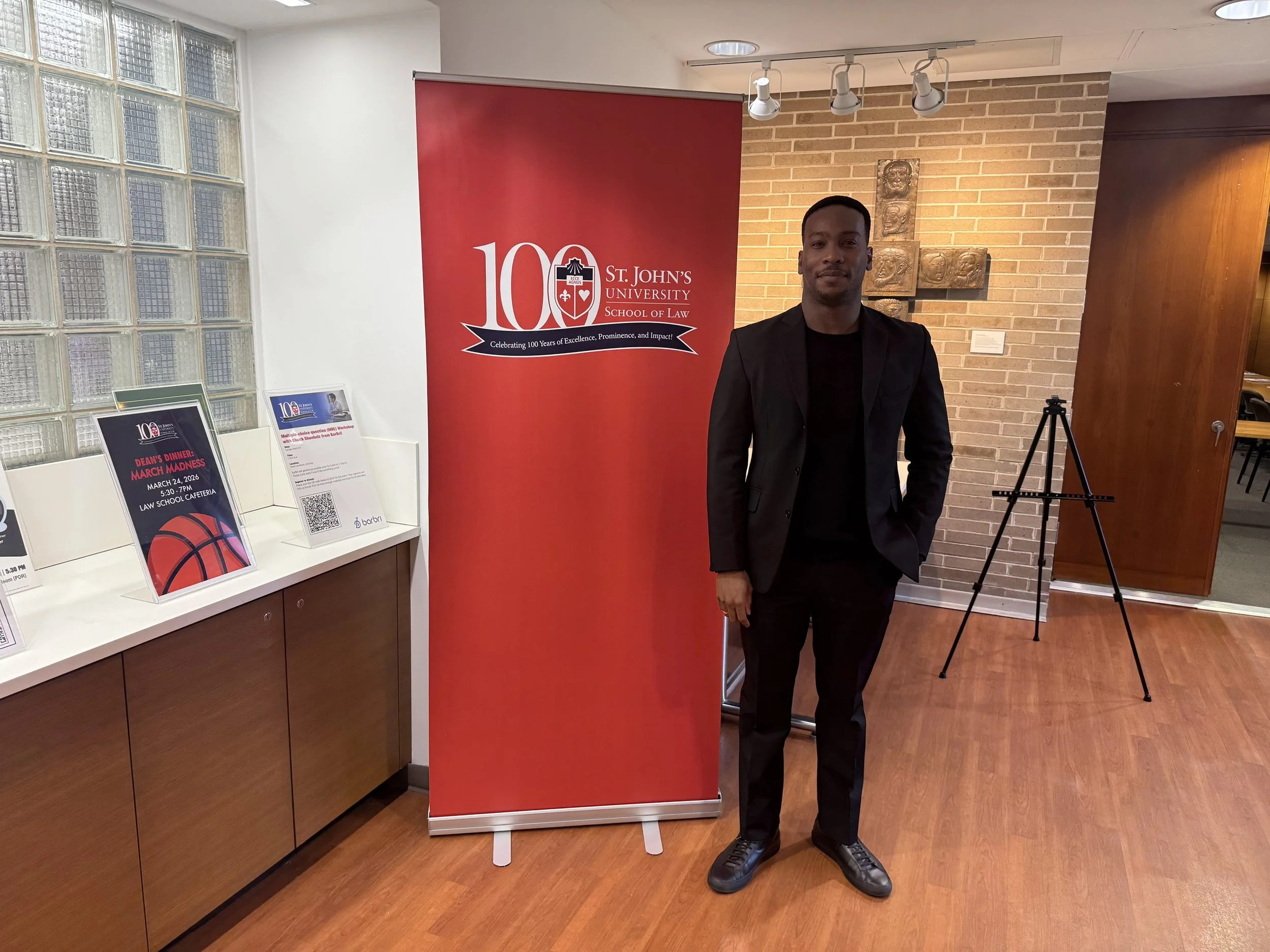 Joshua Scarlett at St. John's University School of Law, with brick and glass block wall behind him.