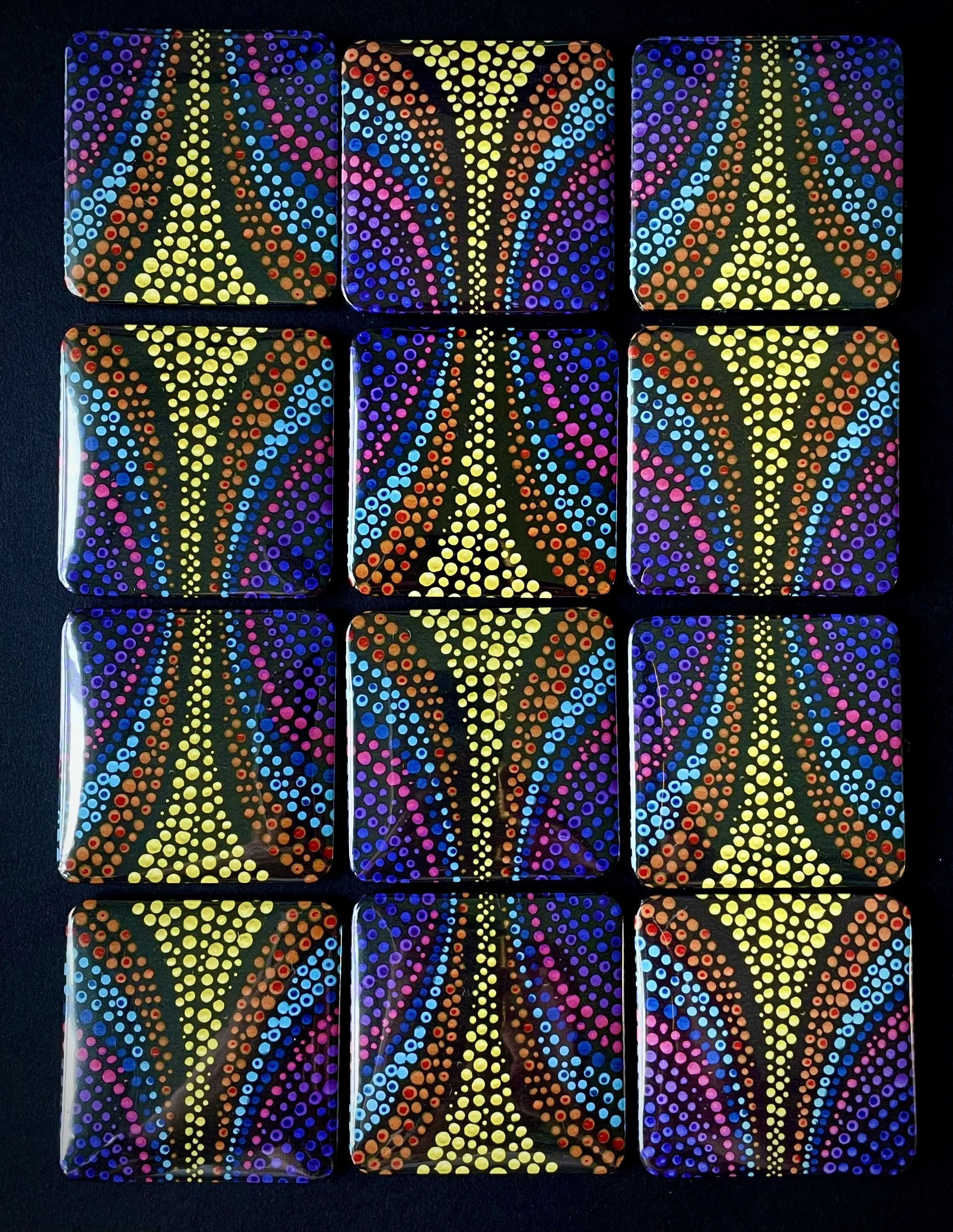 Six painted domino tiles with dots in colors such as yellow, pink, purple, blue, and red arranged in two rows on a black background. The painting features symmetrical, colorful dot patterns forming abstract designs.