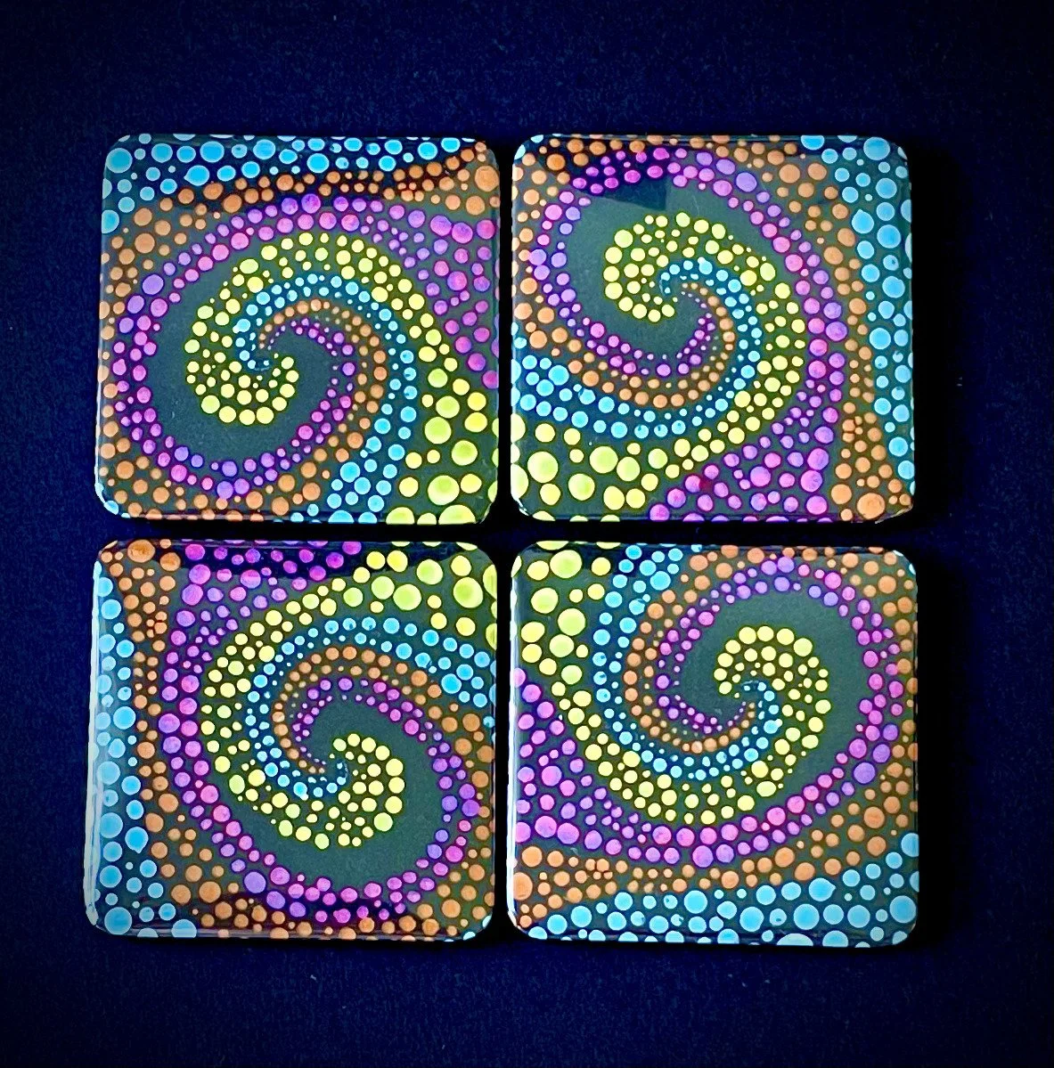 Four square tiles with colorful spirals made of dots in purple, yellow, blue, and orange on a black background.