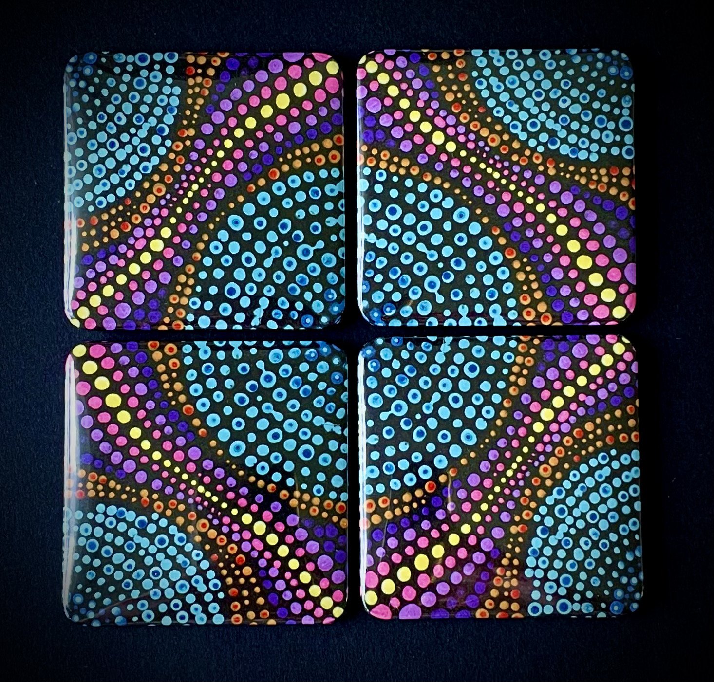 Four square tiles with a colorful dotted pattern, arranged in a 2x2 grid, reflecting on a black surface.