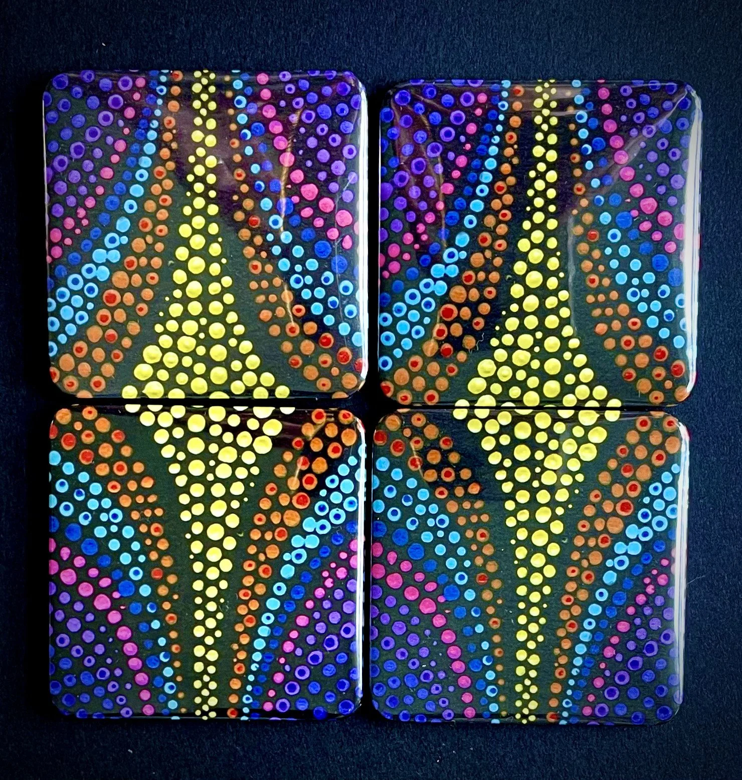 Four square art tiles with colorful dot patterns on a black background, arranged in a 2x2 grid.