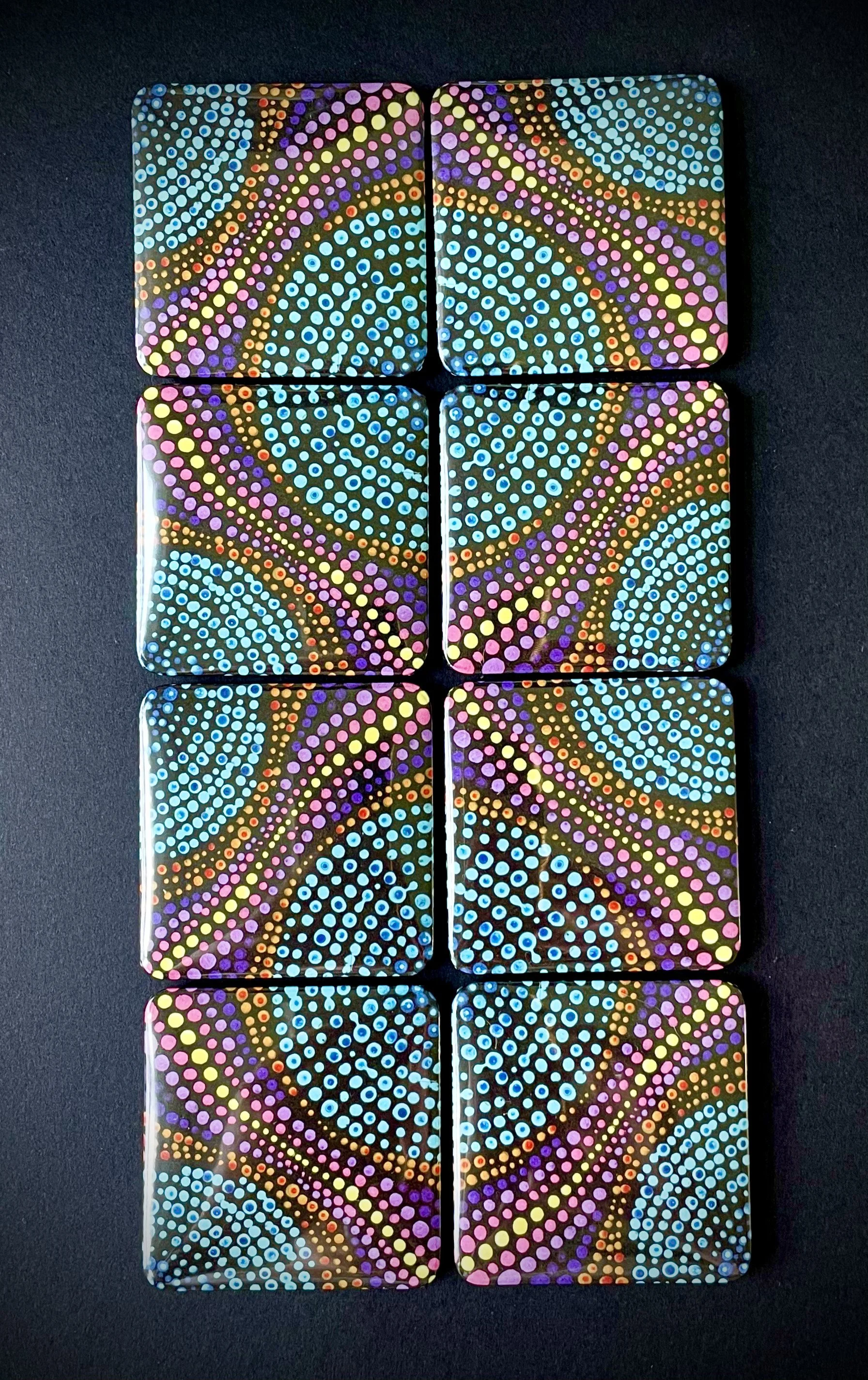 A set of nine black tiles with colorful dotted spiral patterns in pink, blue, yellow, red, and purple, arranged in a 3x3 grid on a black background.