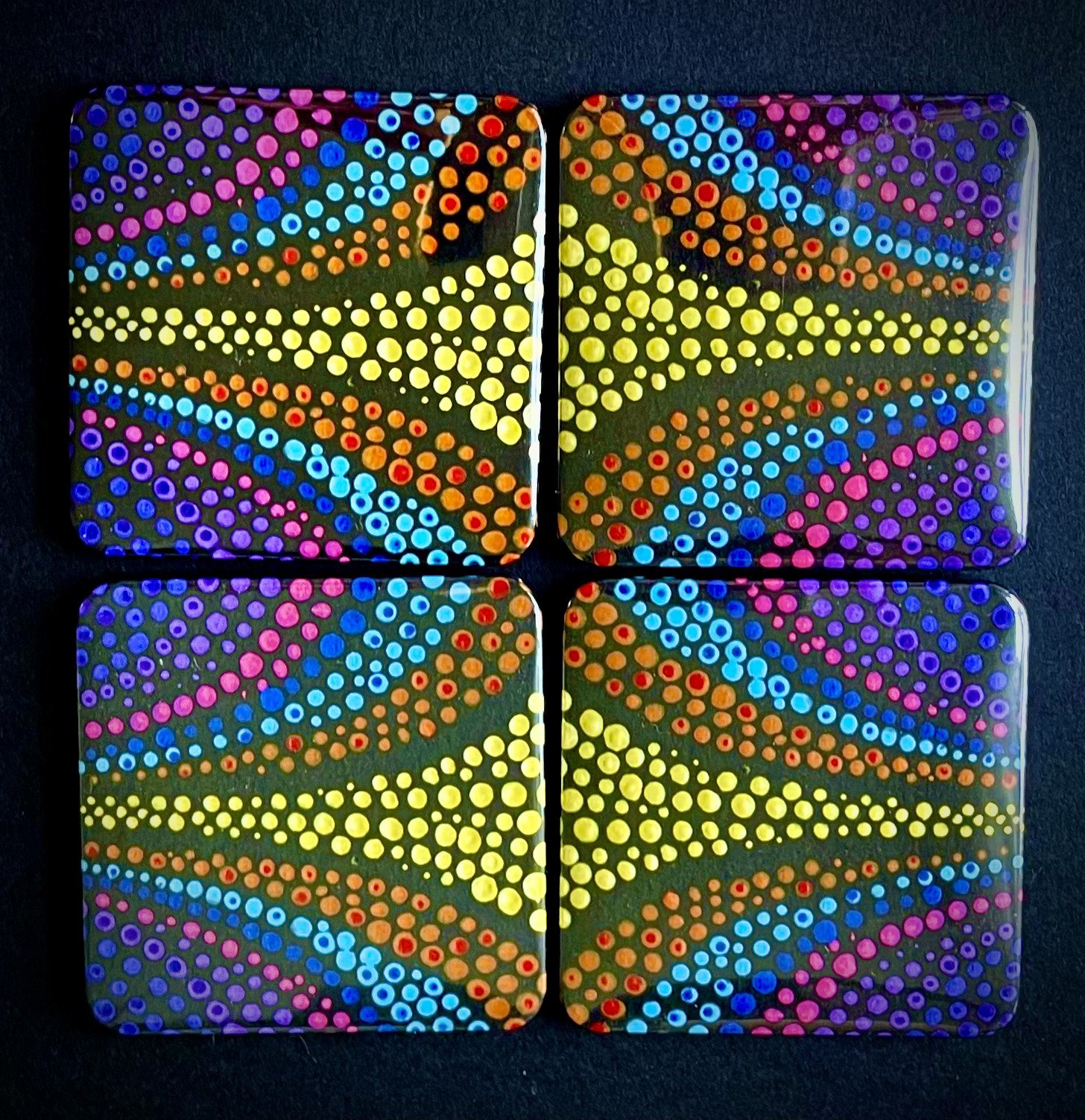 Four square tiles with colorful dotted patterns arranged in a 2x2 grid. Each tile has a black background with vibrant dots forming swirling patterns in pink, blue, yellow, orange, and purple colors.