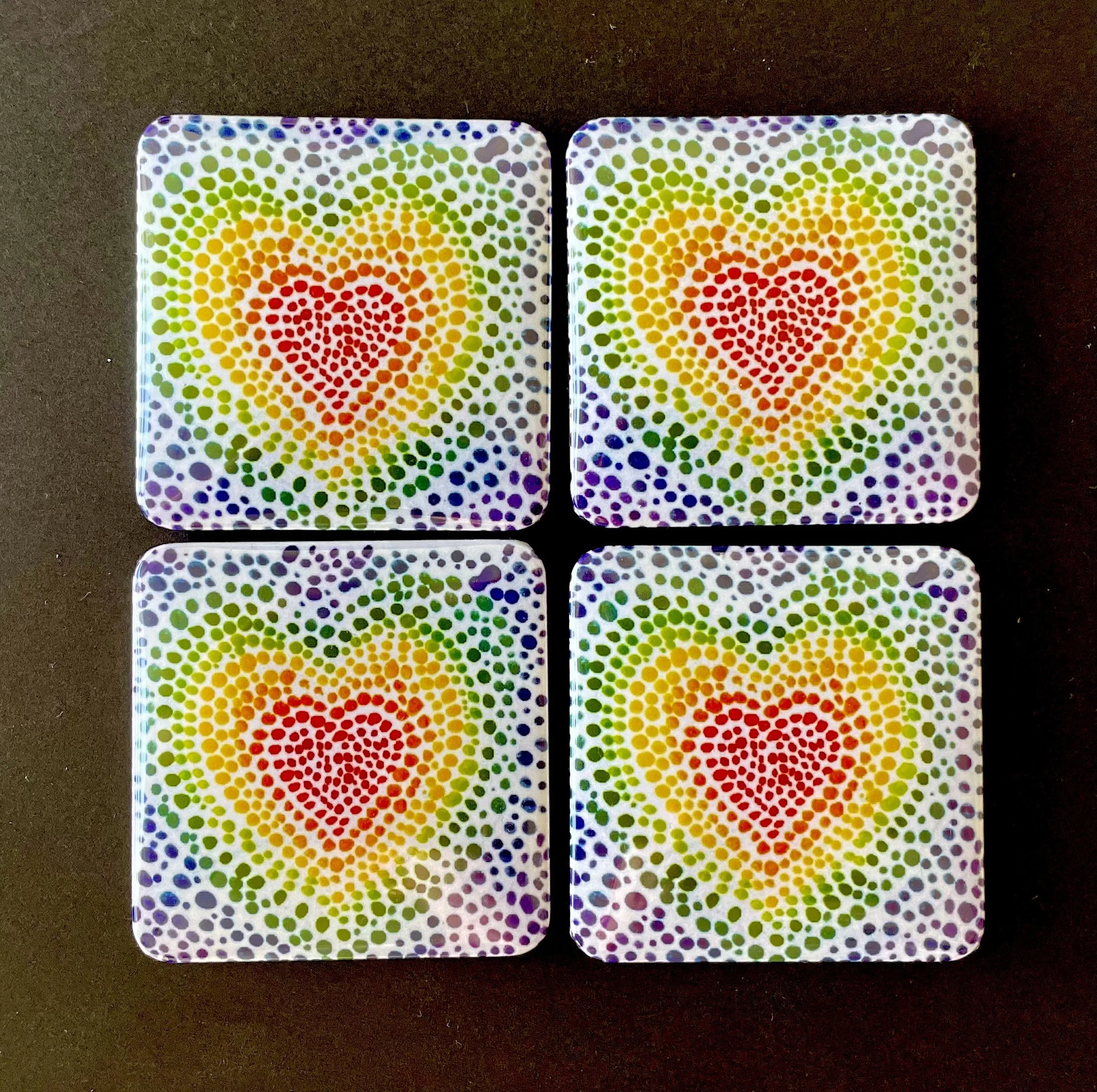 Two square coasters with rainbow-colored dot patterns on a dark surface.