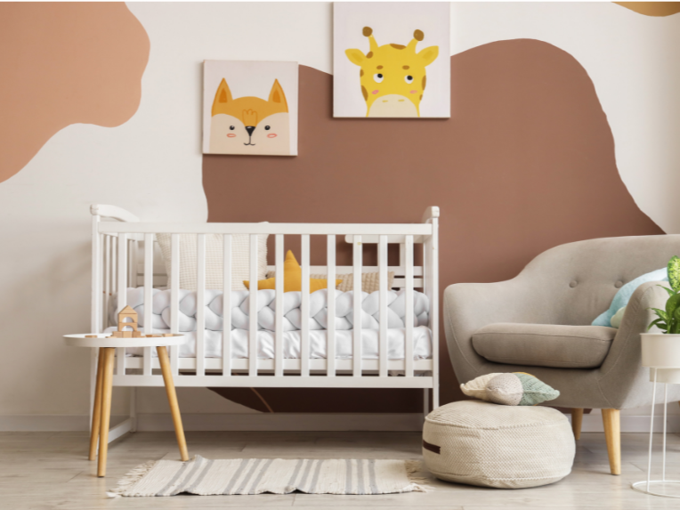 A nursery with a white crib, beige chair, and wall art featuring a cat and a giraffe.