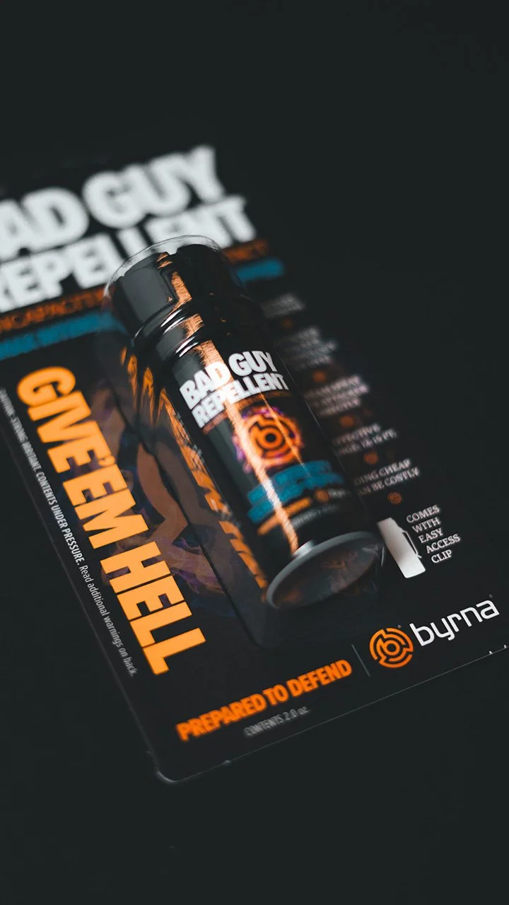 A bottle of BAD GUY REPELT and a logo of Bymra on a promotional card with the slogan PREPARED TO DEFEND.