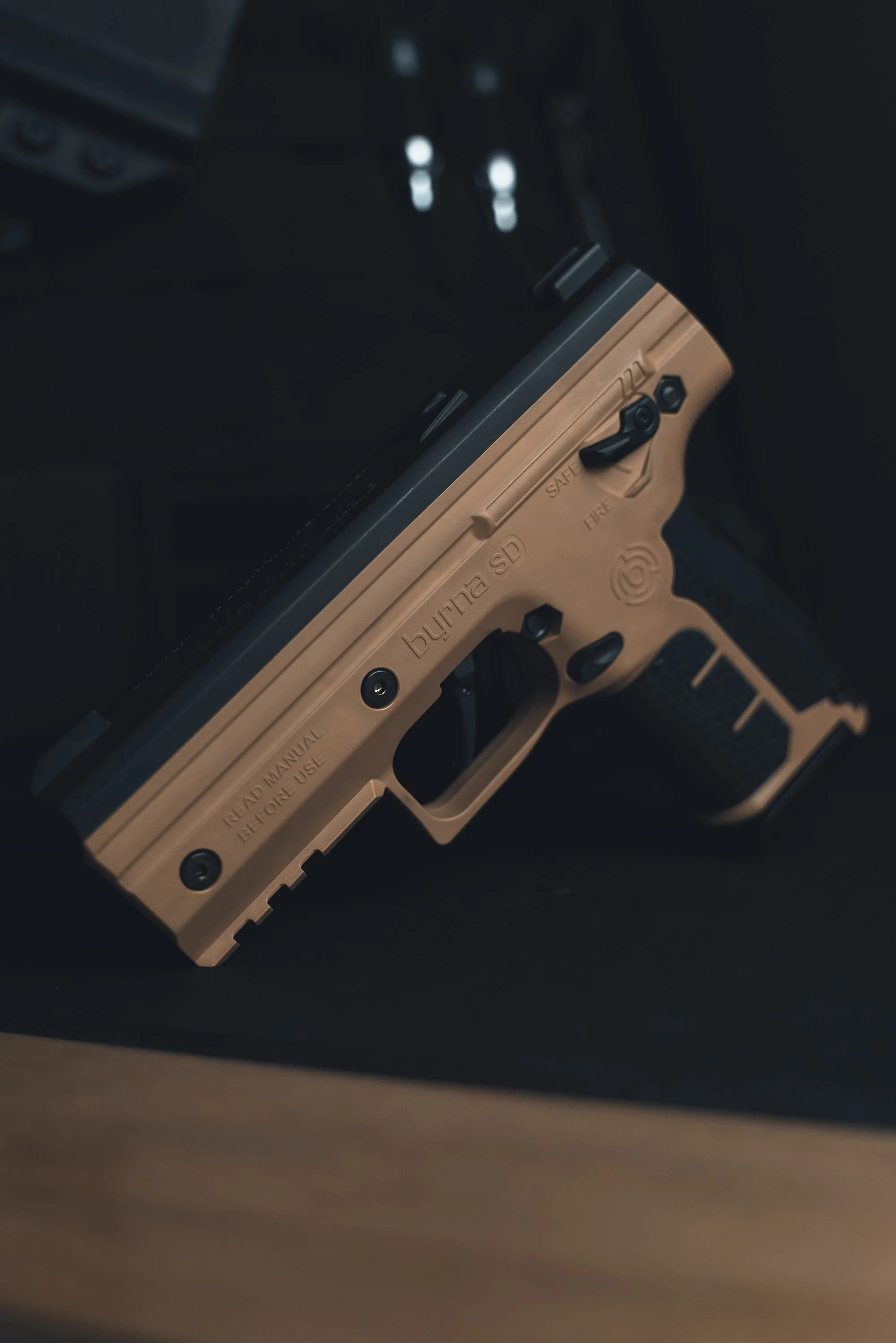 Close-up of a tan firearm slide and trigger mechanism, with text labeling parts such as safety, guard, and manual.