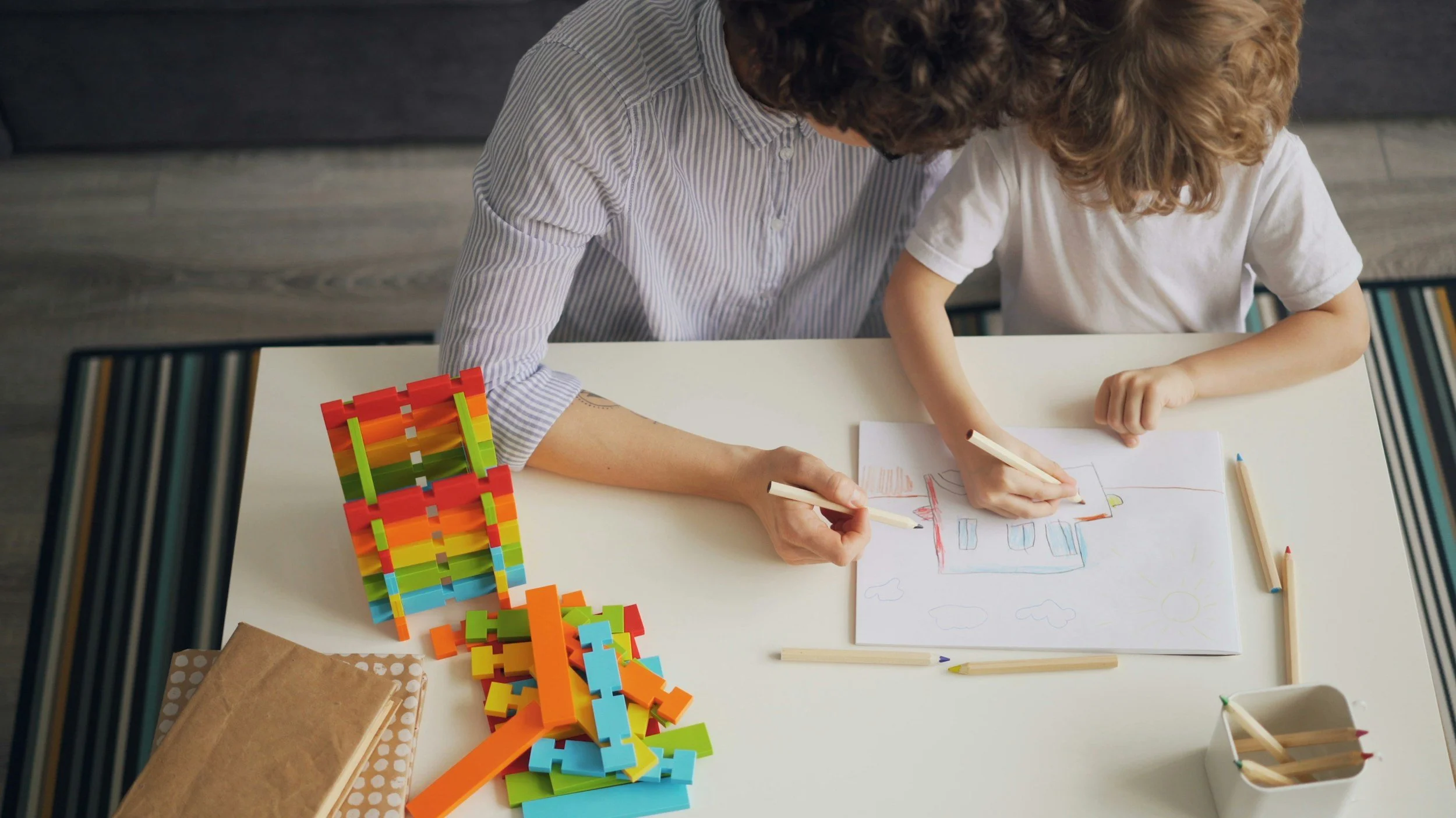 A person and a child drawing together at a table, with colorful building blocks on the side.