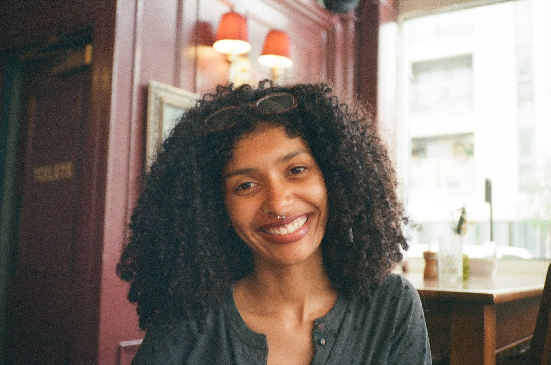 Sorahya in a cozy indoor setting with purple walls, a picture frame, wall lamps, and a large window in the background.