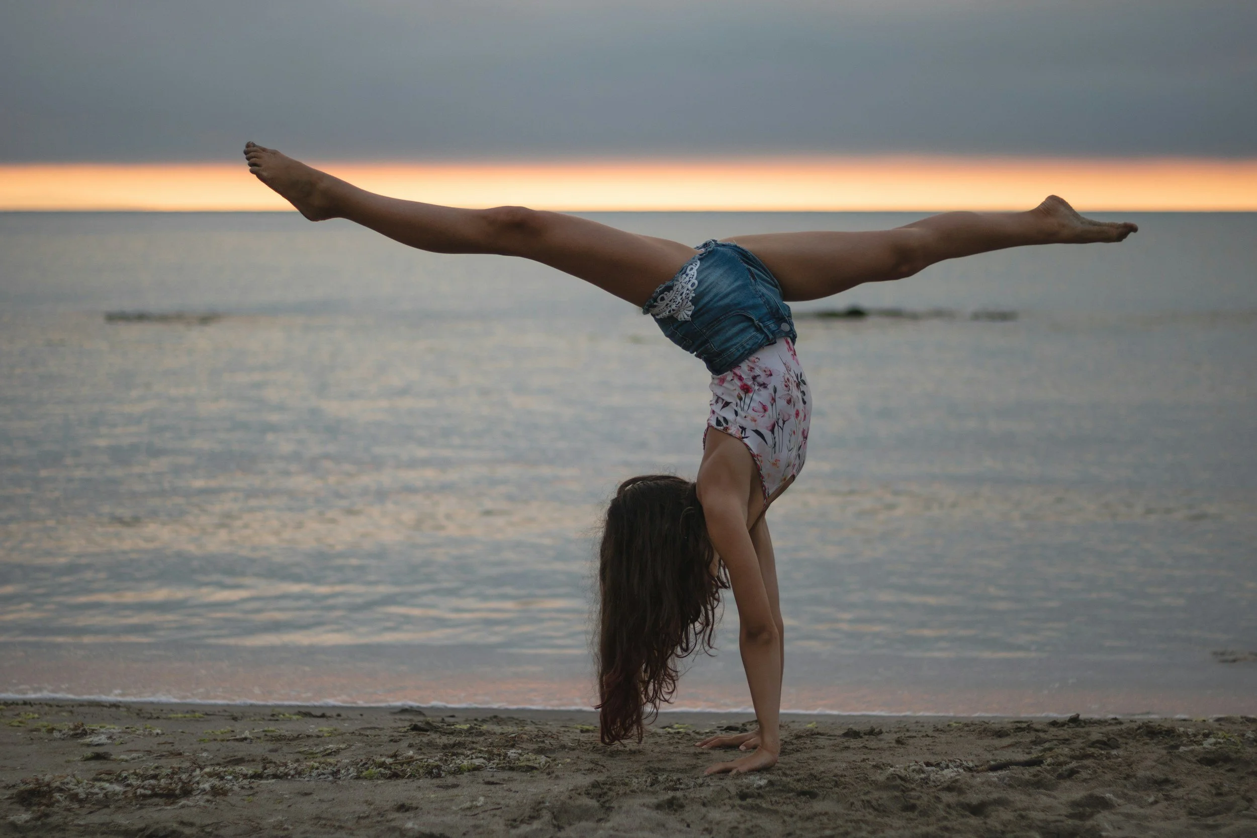 A person performing a handstand on the beach during sunset, with the ocean in the background.
