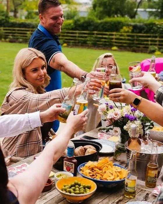 People celebrating outdoors with drinks, food, and flowers at a gathering.
