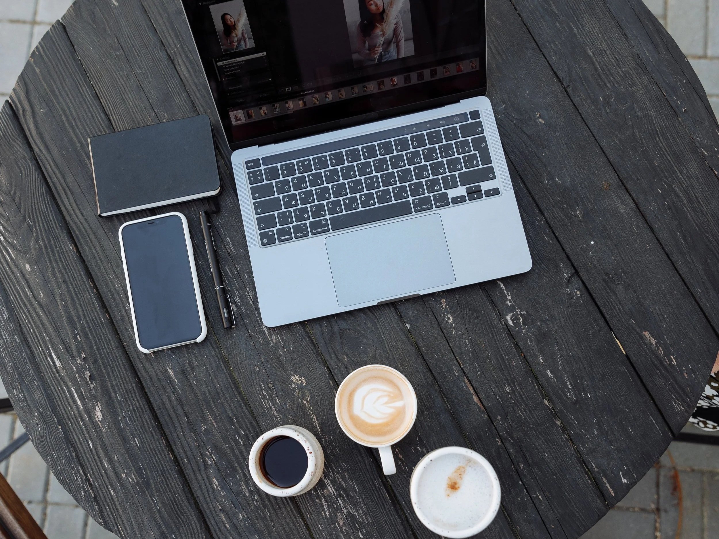 Laptop, smartphone, notebooks and coffee cups arranged on a wooden table.