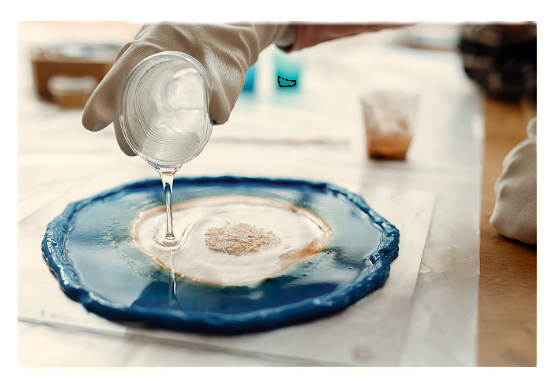 Person pouring liquid onto a blue and white ceramic piece in a workspace.