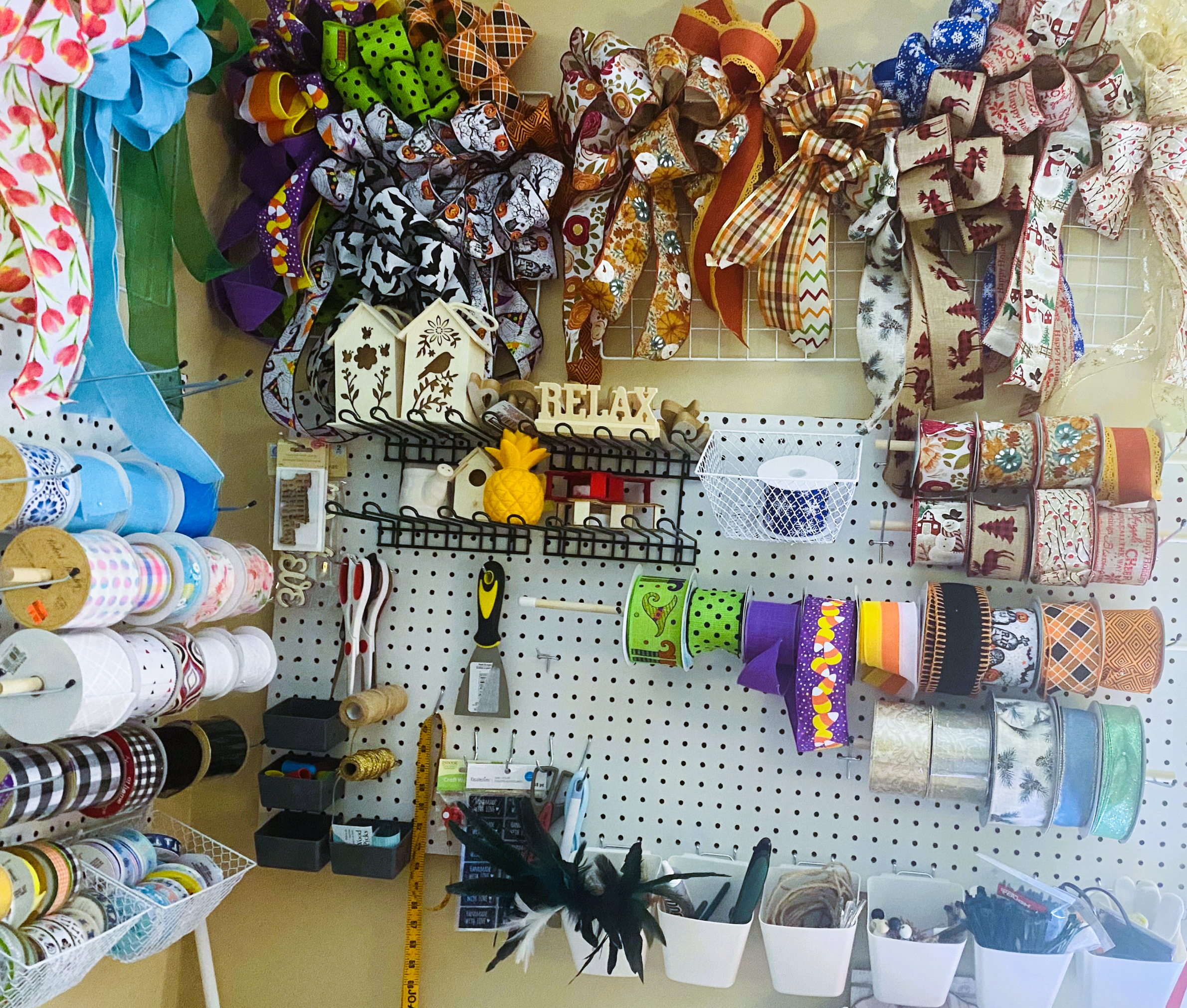 Display of various holiday ribbons, decorative tapes, scissors, and craft supplies on a pegboard and shelves.
