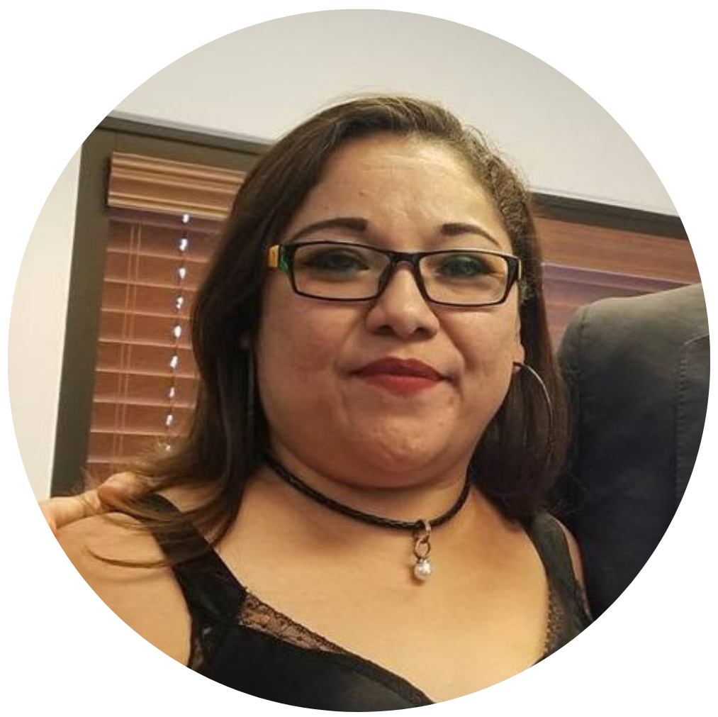 Mujer con gafas, cabello castaño oscuro, vistiendo top negro con encaje, collar con perla y ajustado en un ambiente interior.