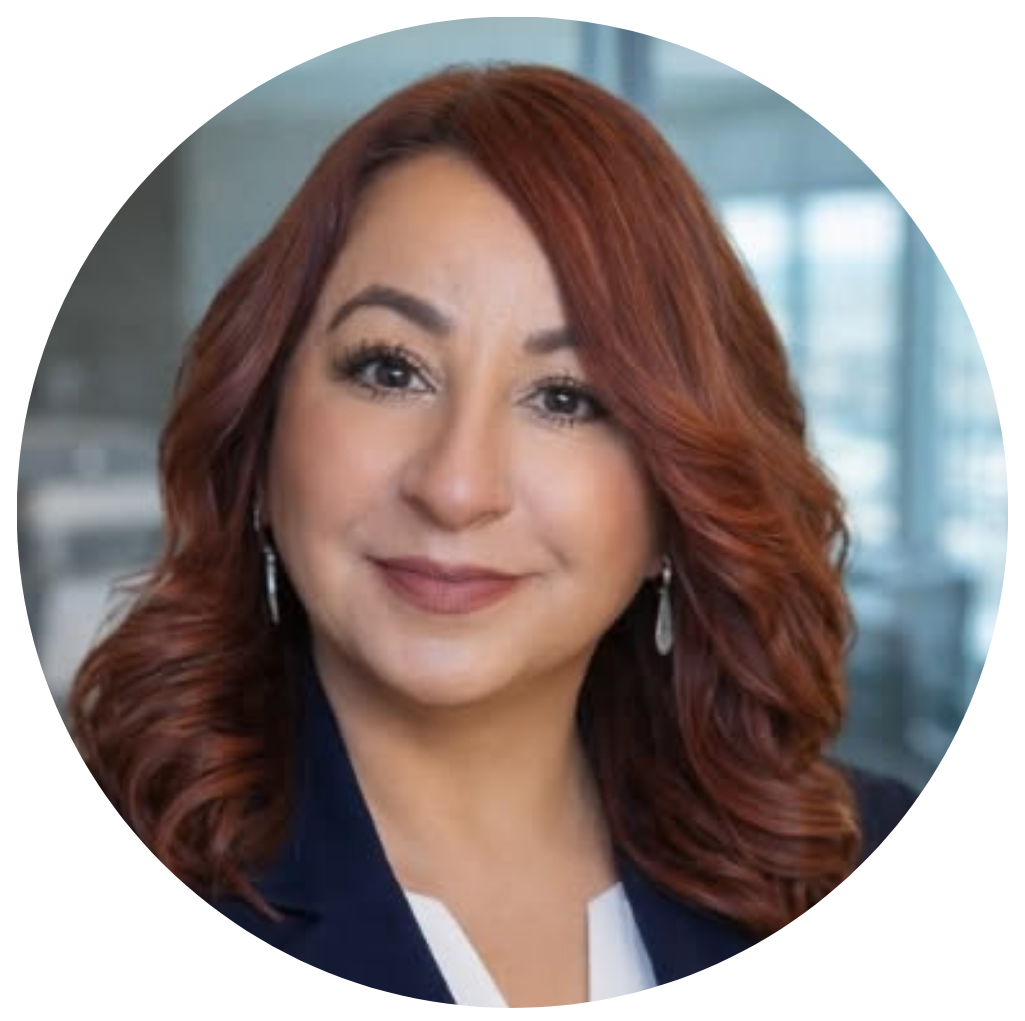 Retrato de una mujer con cabello rizado y rojo, vestida con traje profesional en un entorno de oficina, sonriendo suavemente.