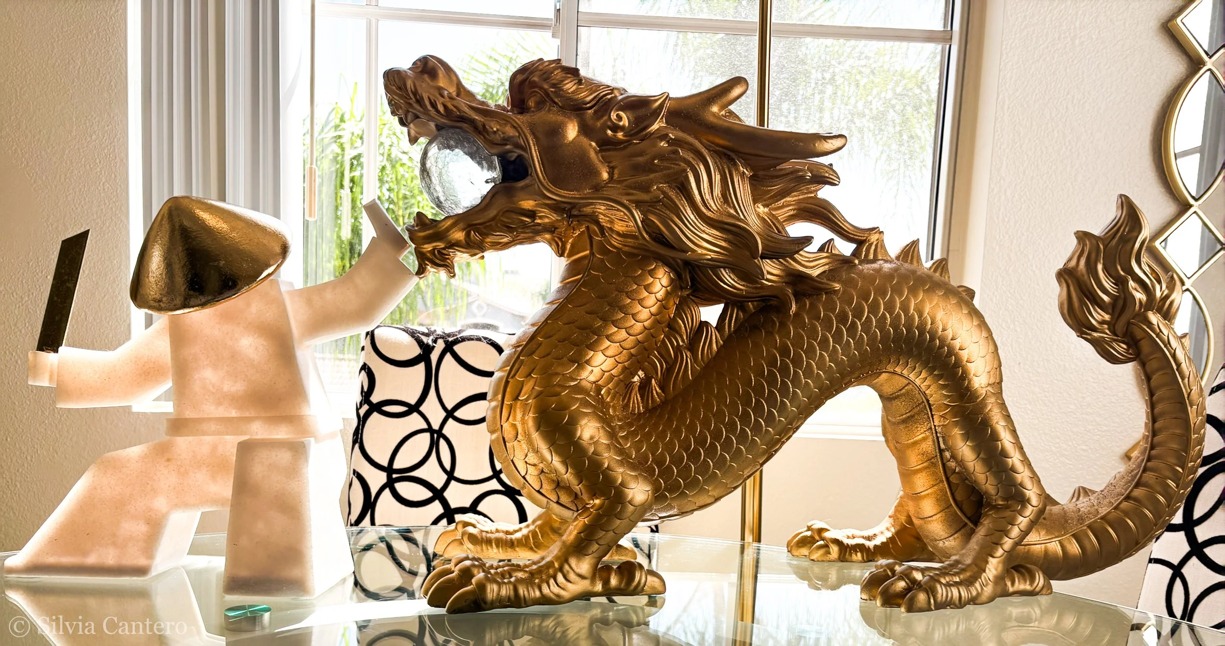 Decorative golden dragon sculpture with intricate scales and flowing mane, placed on a glass surface near a window.