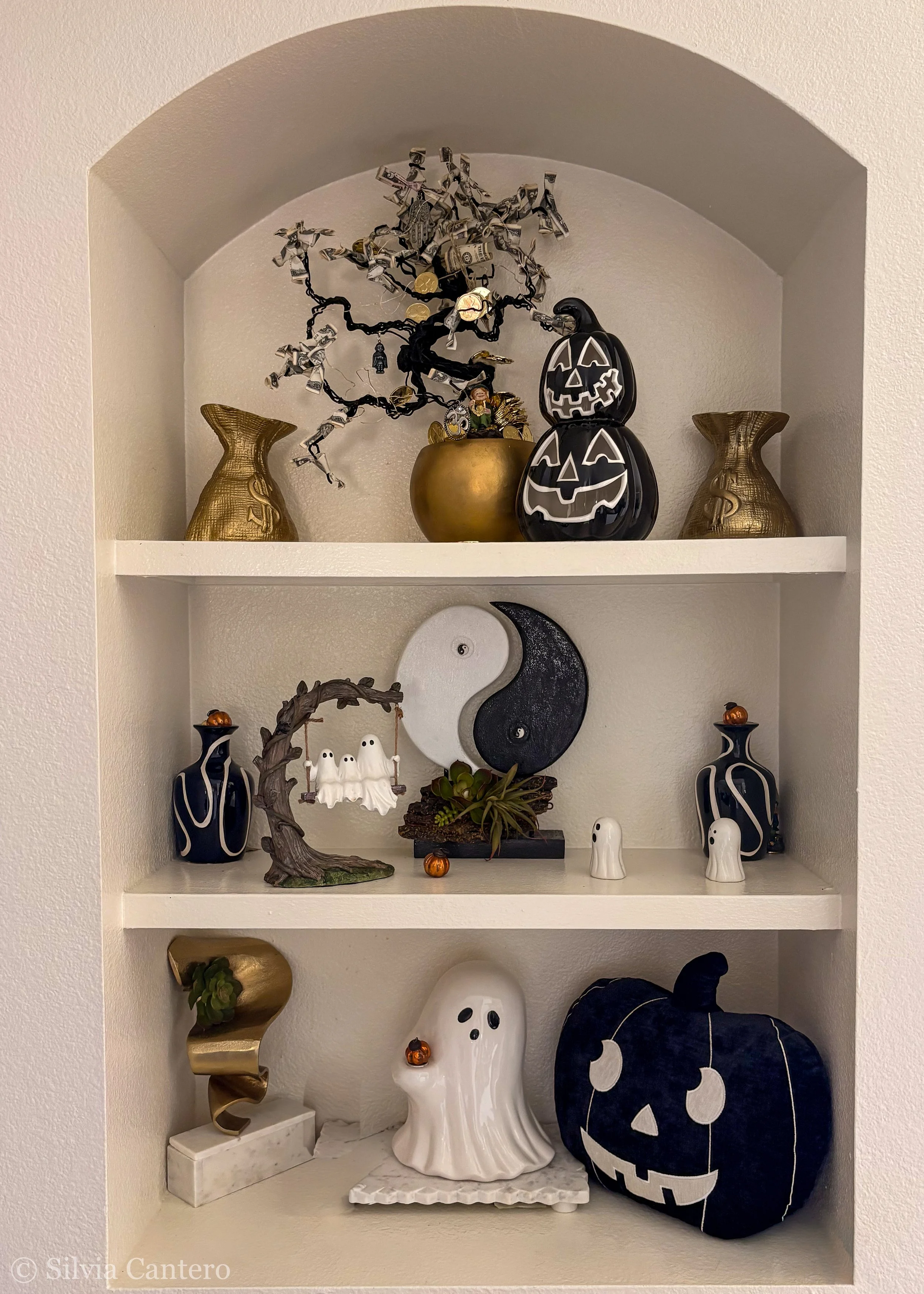 Decorative Halloween-themed display with a black and white pumpkin-shaped lantern, a ghost figurine, a black and white moon and star-shaped pillow, and various small Halloween ornaments on shelves.