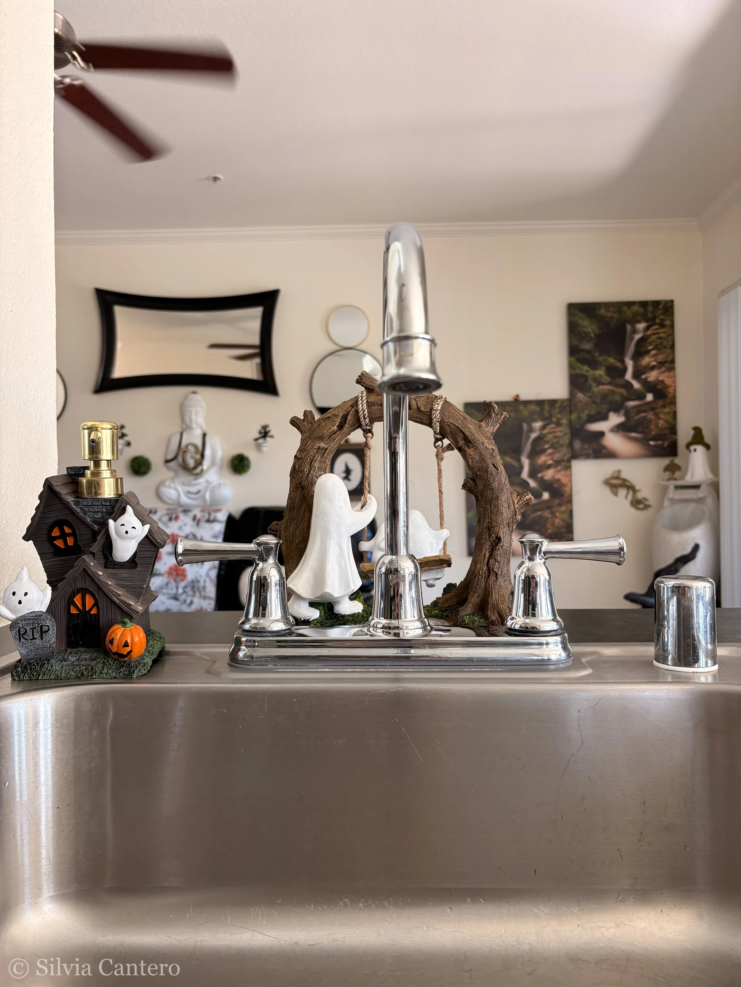 Halloween-themed kitchen sink decor with a haunted house, ghost figurines, pumpkins, and spooky scenery in the background.