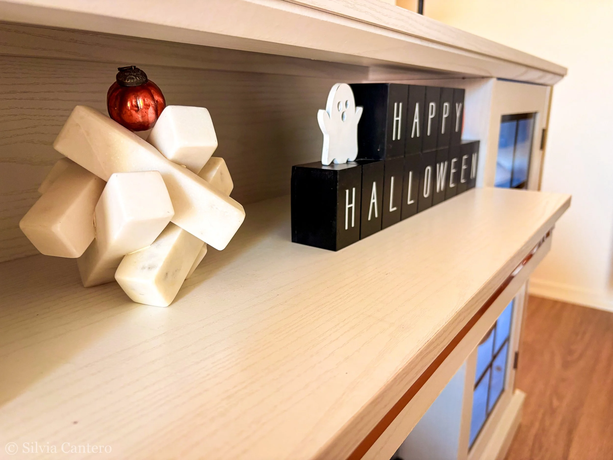 Decorative pumpkin, white wooden star, and black blocks spelling out 'HAPPY HALLOWEEN' on a light wood shelf.