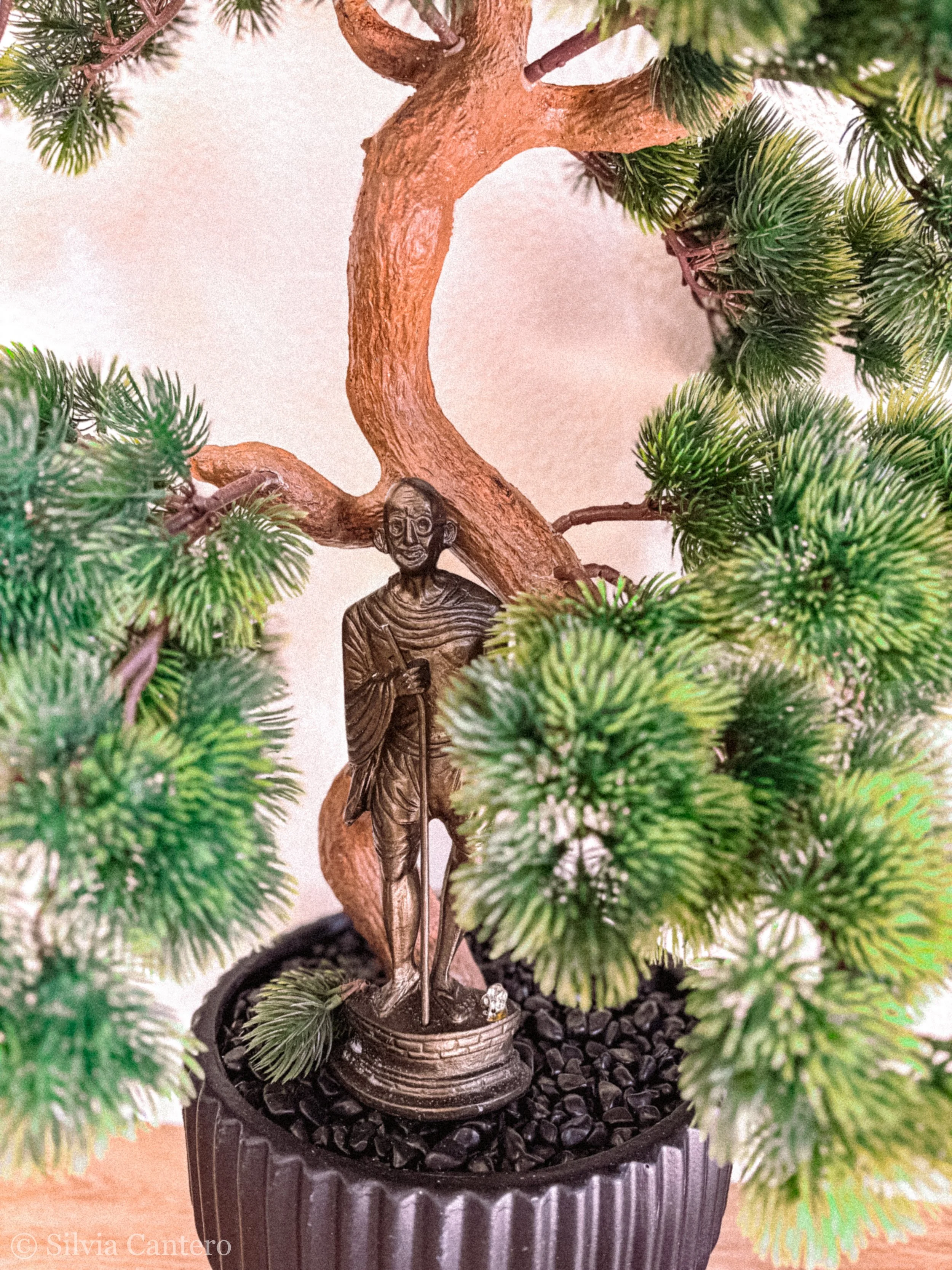 A small potted artificial Christmas tree with green branches and a metal figure of an elderly man with a beard, dressed in clothing from the 18th or 19th century, positioned among the branches.