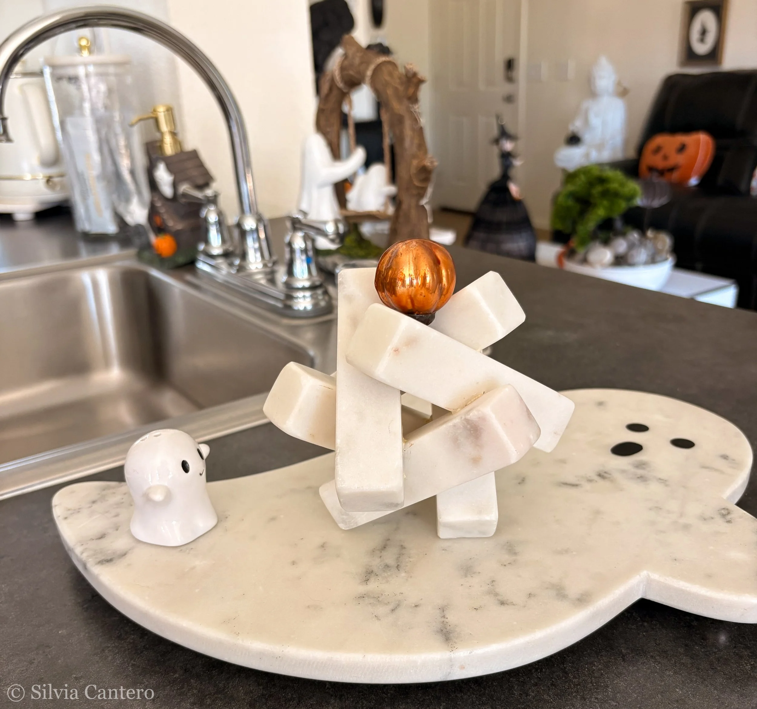 Decorative art piece with a copper-colored sphere on top, surrounded by geometric marble-like shapes, placed on a marble base in a kitchen.