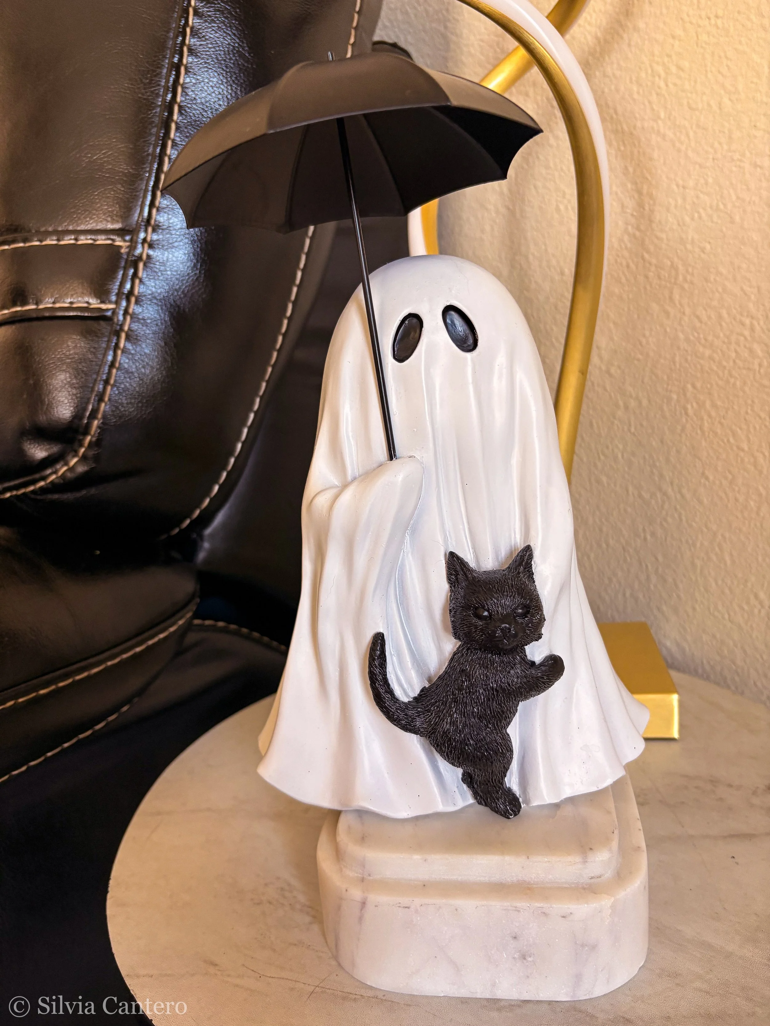 Decorative figurine of a ghost holding a black umbrella with a black cat at its base, displayed on a beige surface.