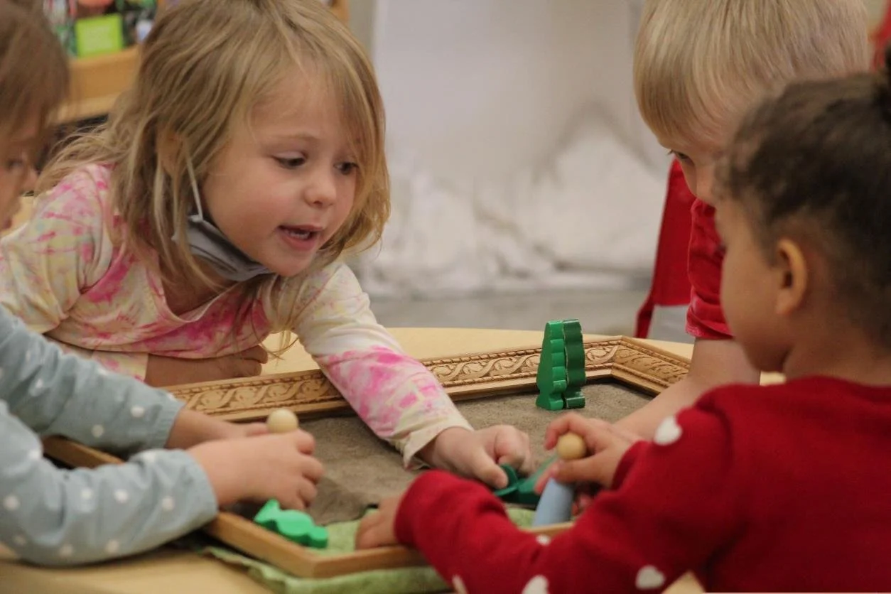 Four young children playing a tabletop game with green and wooden pieces.