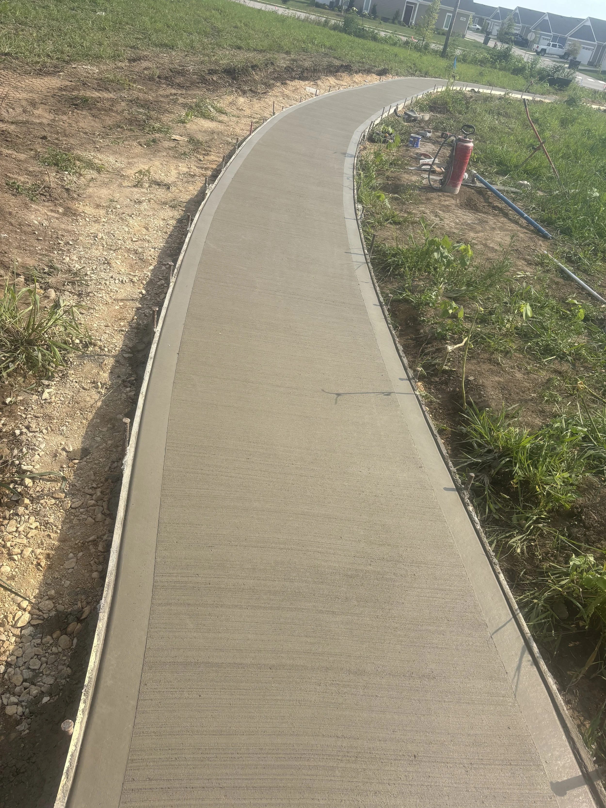 Newly paved sidewalk curving through a grassy area with some construction tools and equipment alongside.