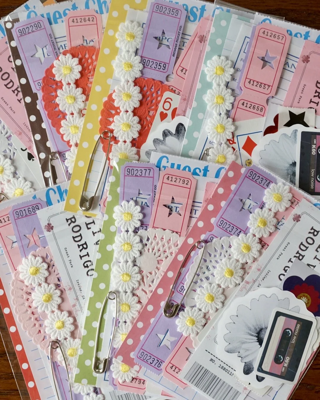 Several colorful guest checks or receipts decorated with daisy flower doilies and safety pins, scattered on a wooden surface.