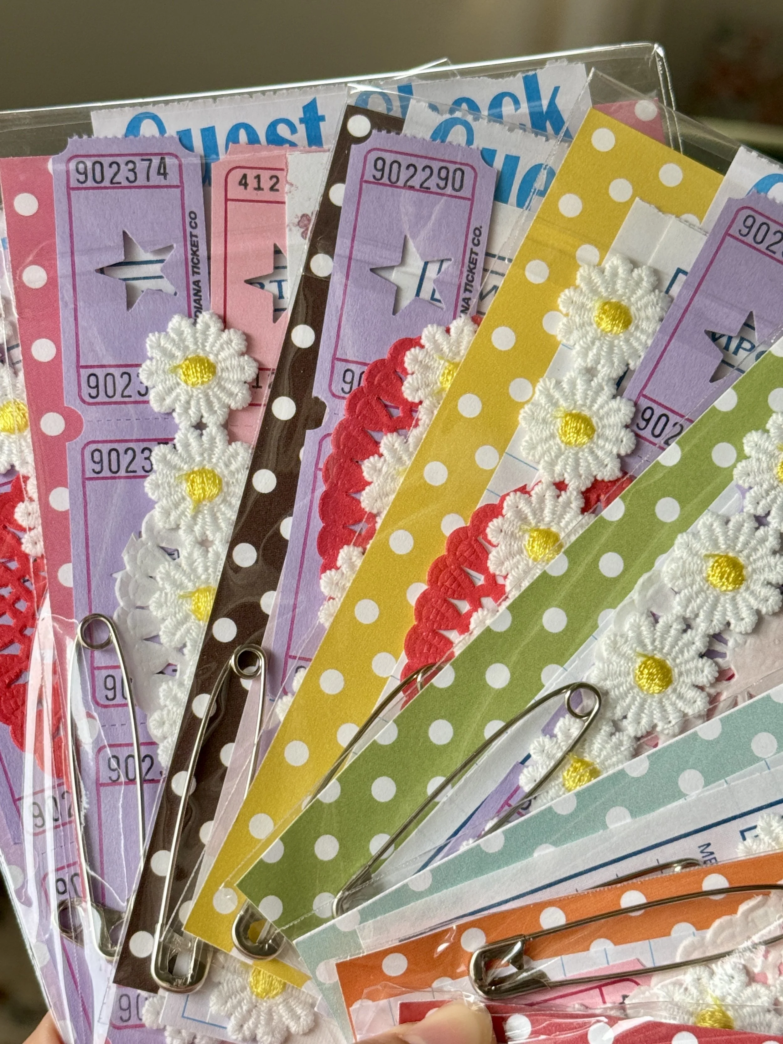 Collection of decorative paper clips with colorful patterned paper backing, some with embroidered white daisy flowers attached.