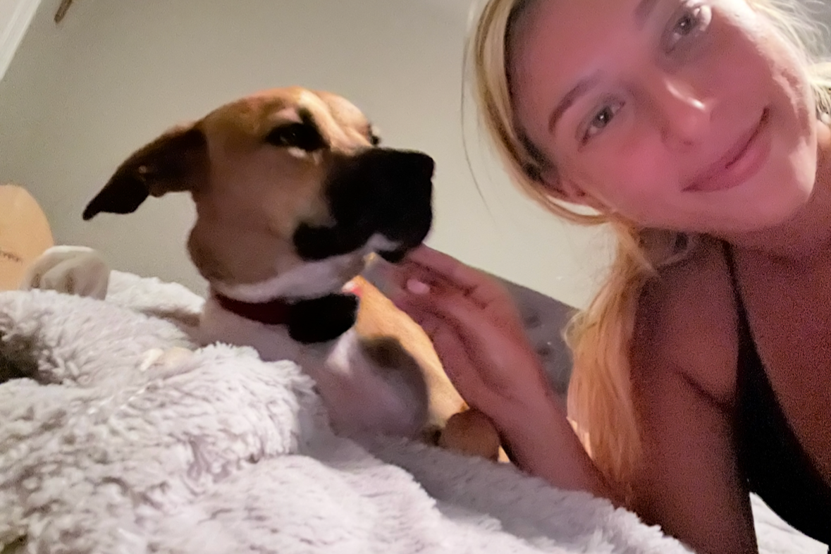 A woman smiling and petting a dog lying on a soft blanket.