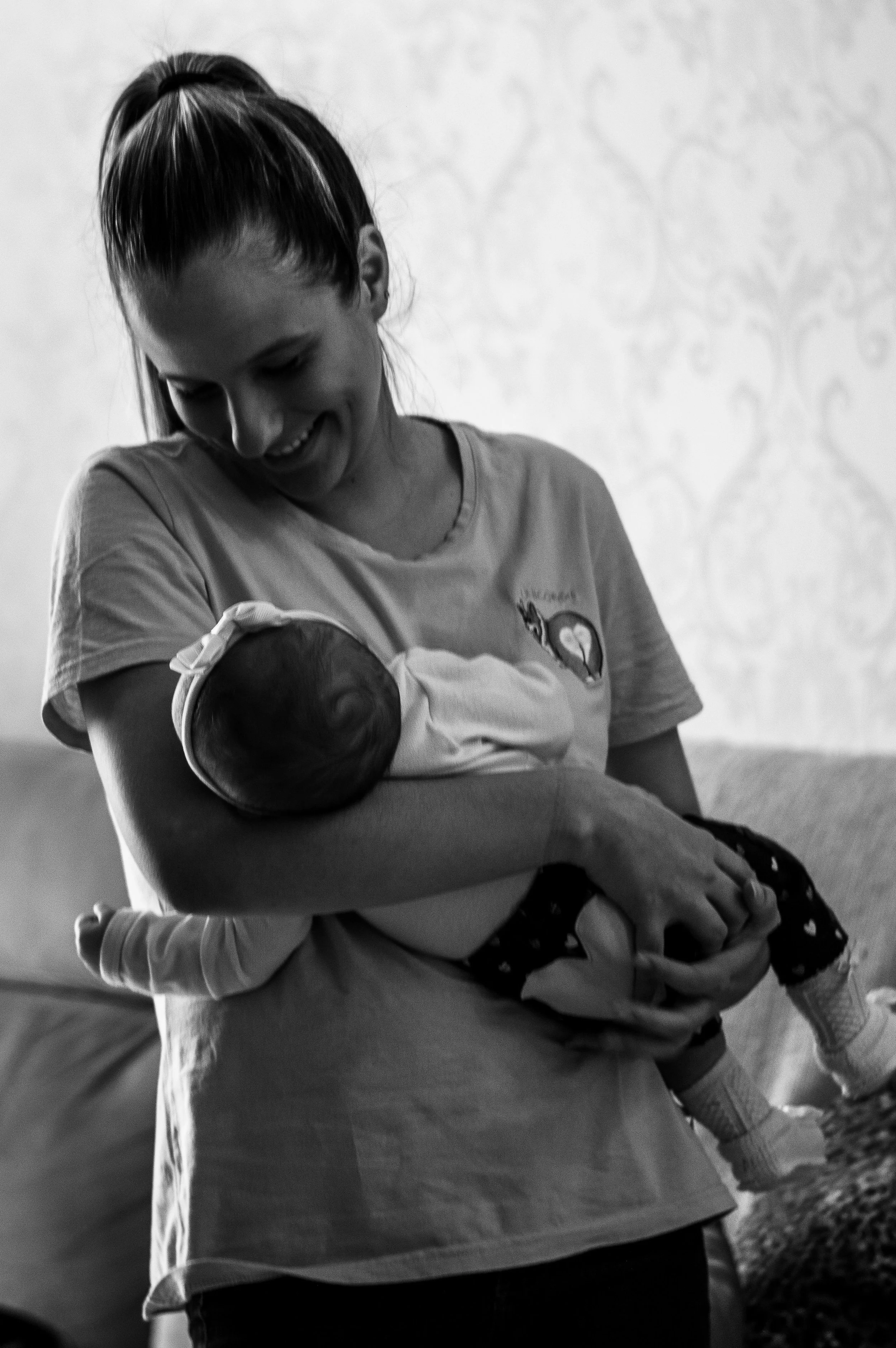 A woman holding a baby in her arms, smiling and looking down at the baby, who is wearing a striped outfit and a hat.