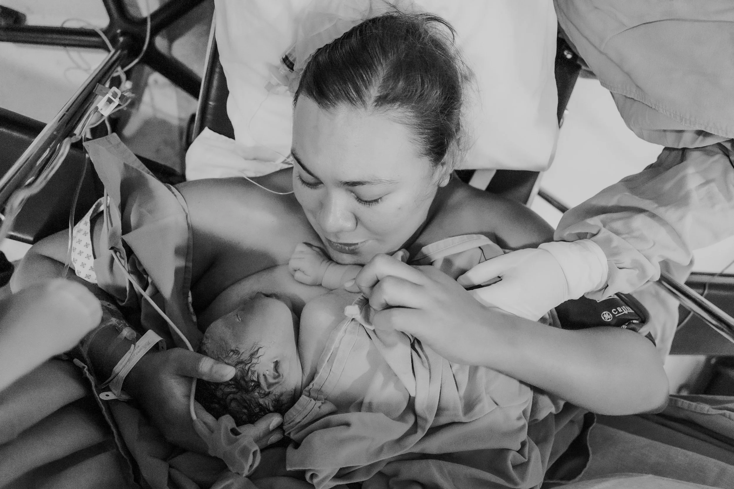 A woman in a hospital bed holding a newborn baby, with medical equipment and IV lines attached.