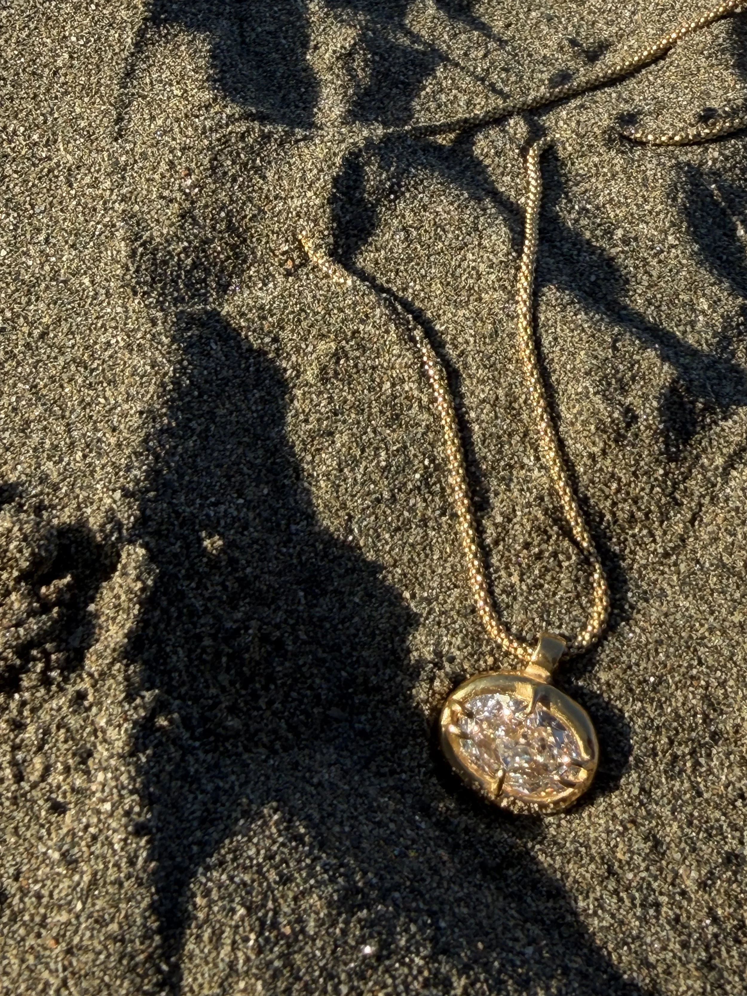 18k 9k yellow gold necklace with oval-cut white diamond pendant in an organic claw setting.