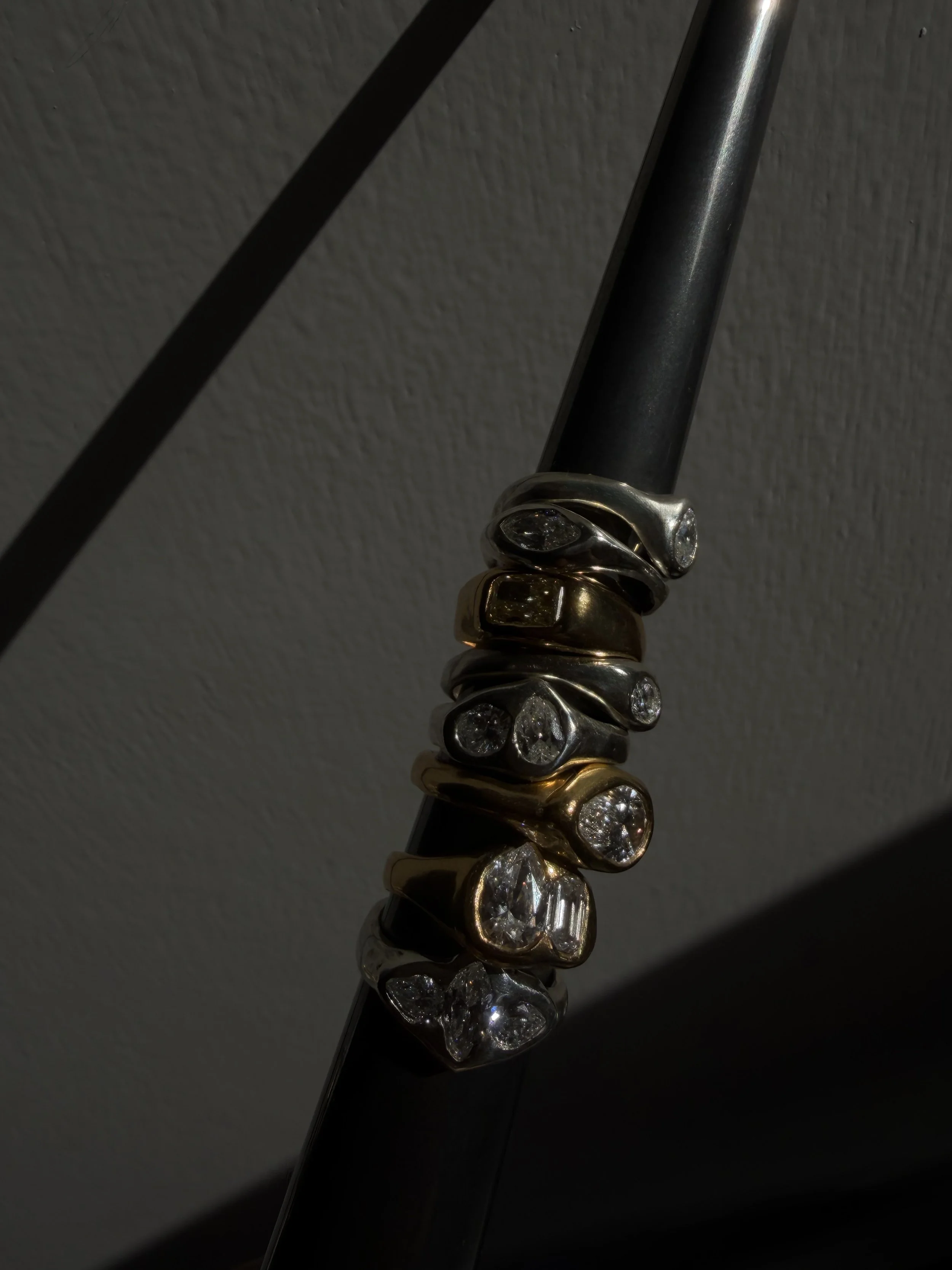 Close-up of a organis ring stack with assorted rings, including yellow gold, white gold, and diamond-encrusted rings, on a dark surface with dramatic lighting.