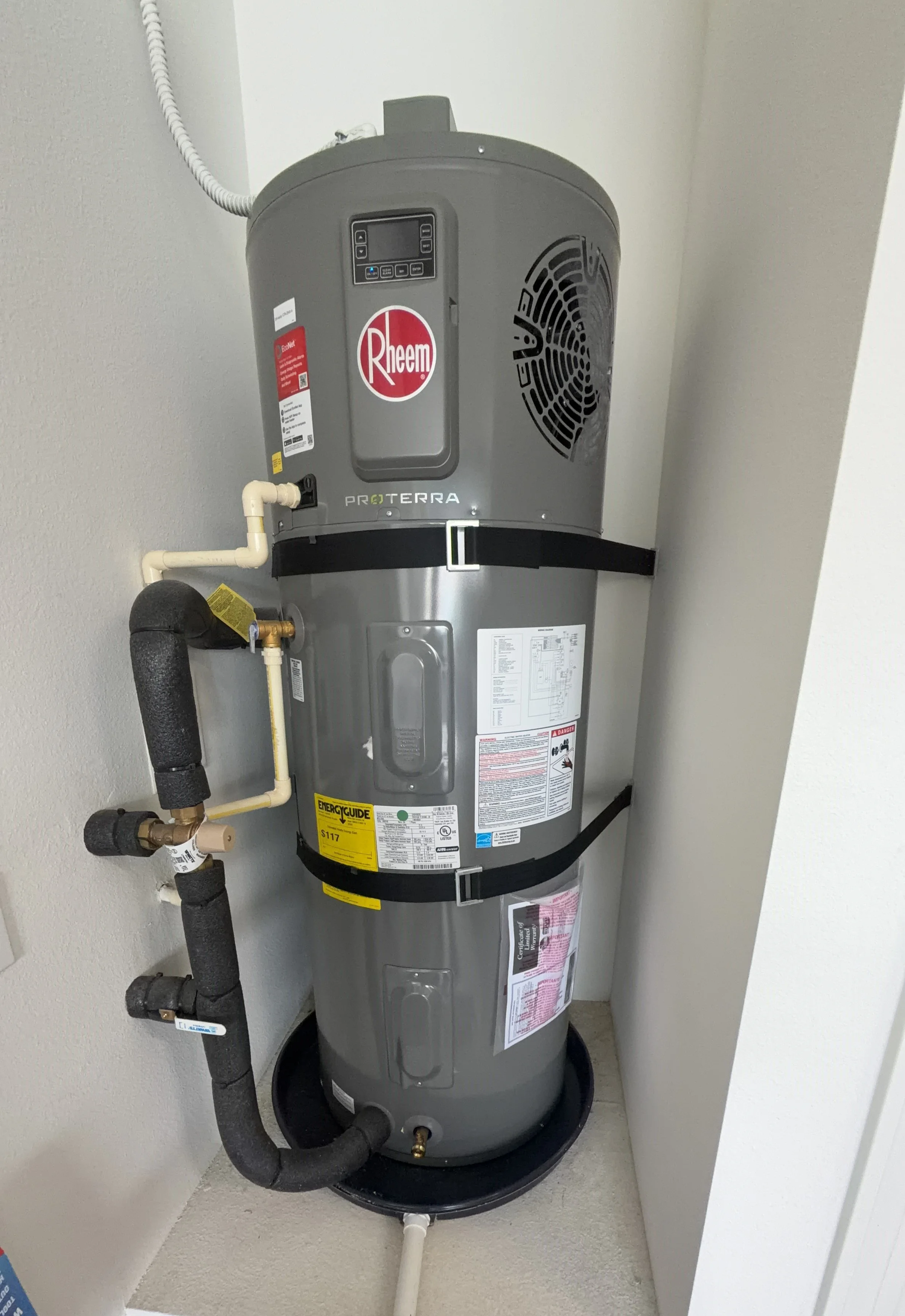 A Rheem Proterra water heater installed in a garage with pipes and electrical connections.