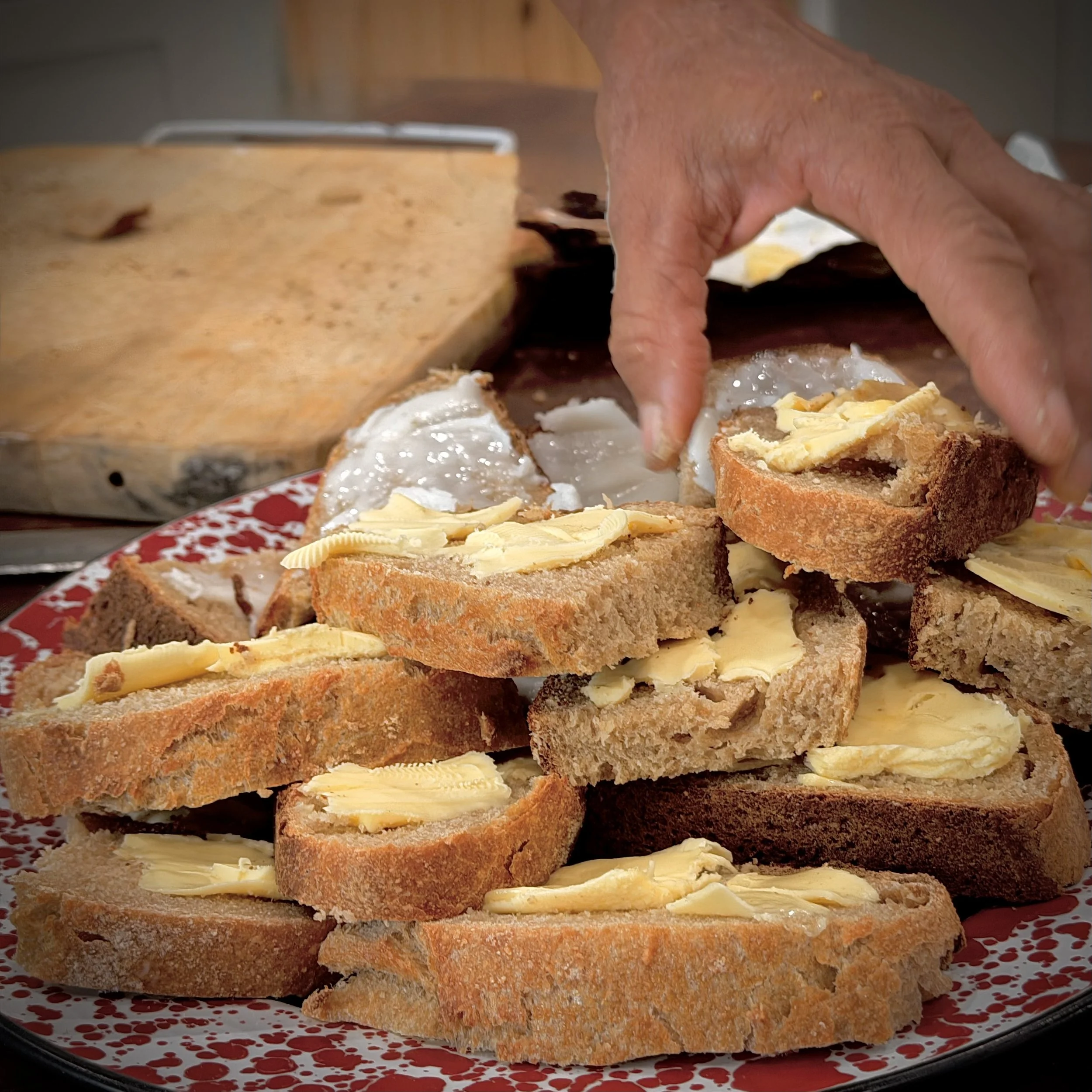 Stacked slices of bread with butter on top, on a red and white speckled plate.