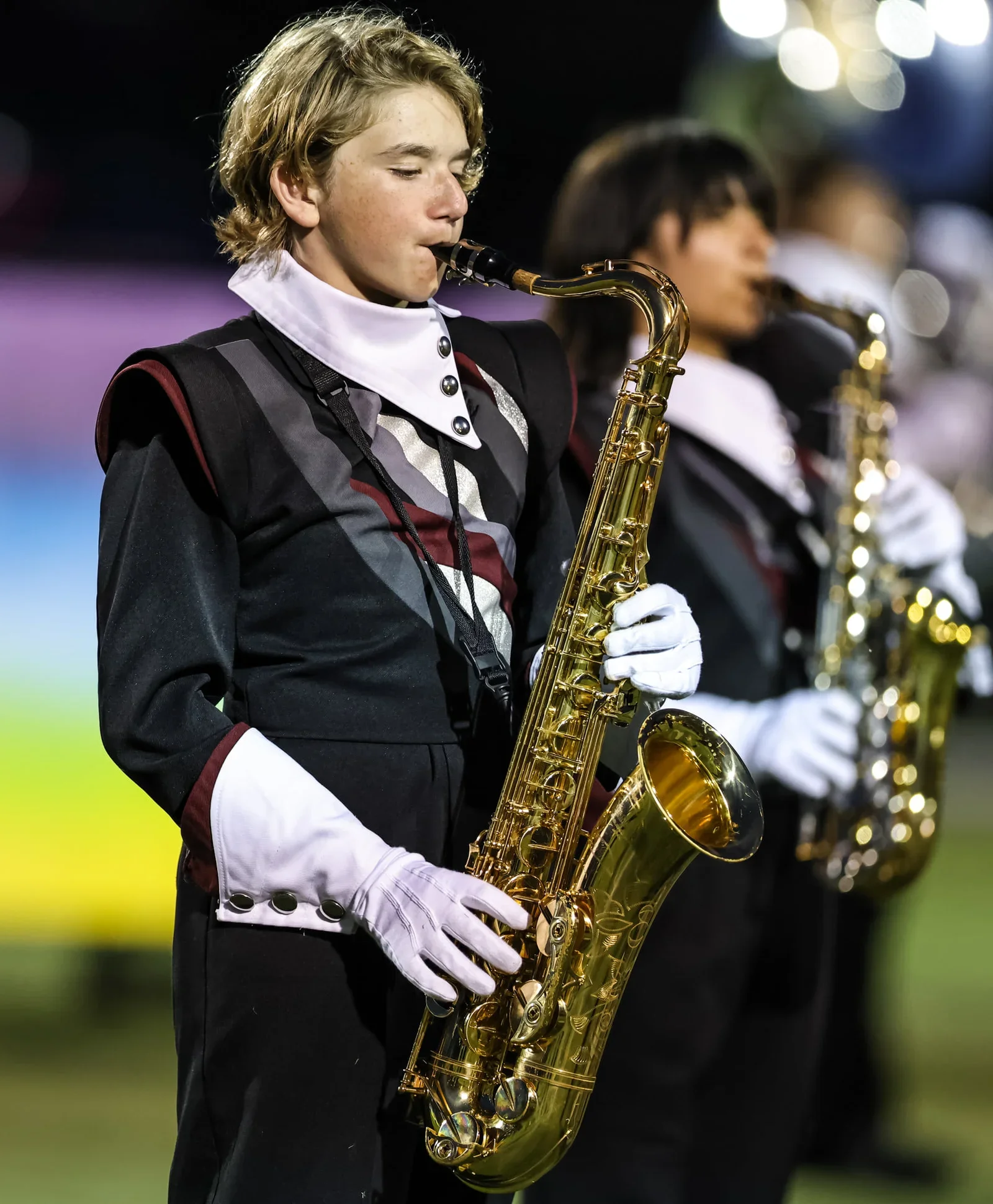 Young band member playing a gold saxophone during a performance, wearing formal black and white attire.